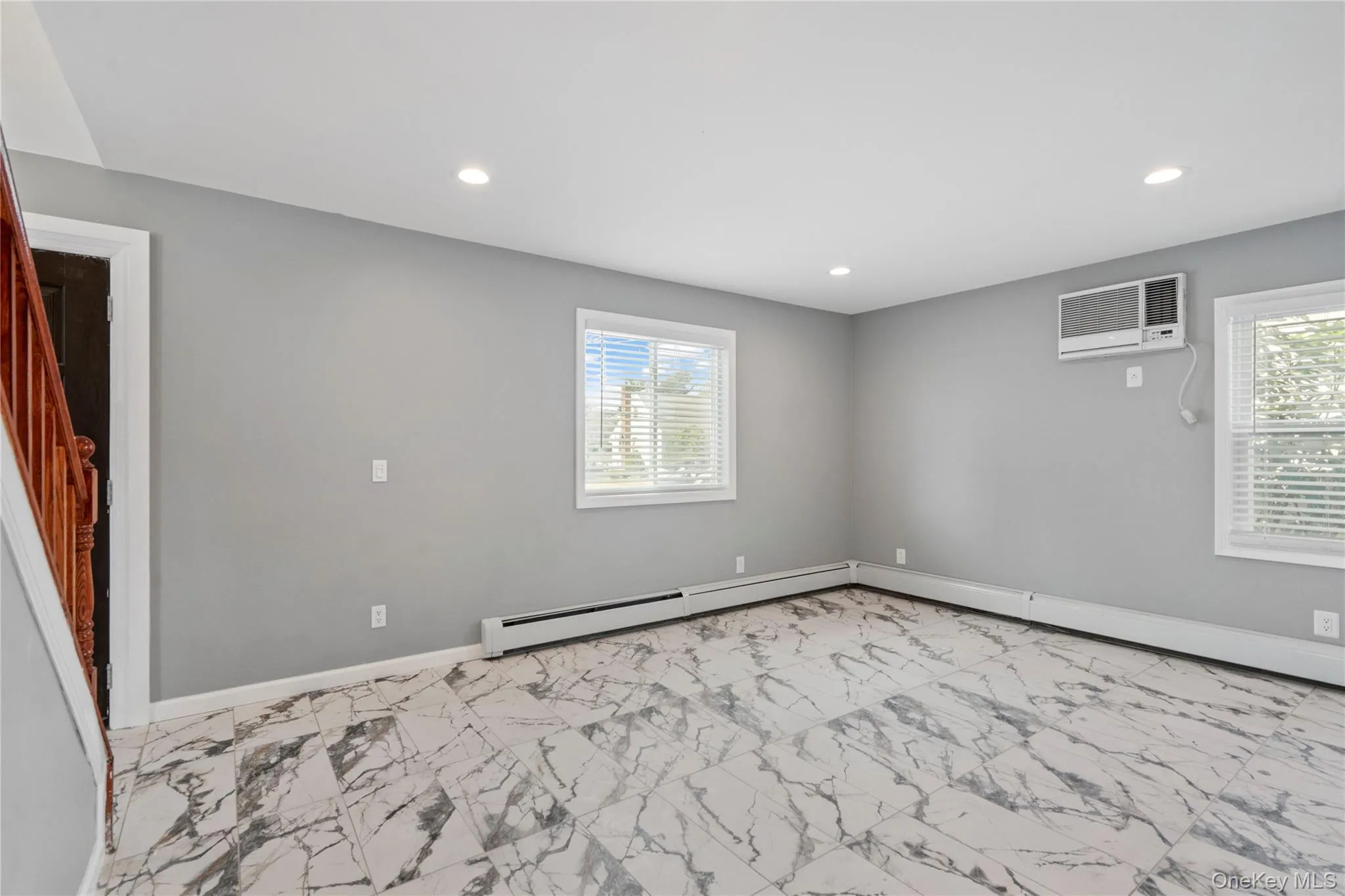 Spare room with light marble finish flooring, recessed lighting, a wall mounted air conditioner, stairway, and a baseboard heating unit Spare room with light marble finish flooring, recessed lighting, a wall mounted air conditioner, stairway, and a baseboard heating unit