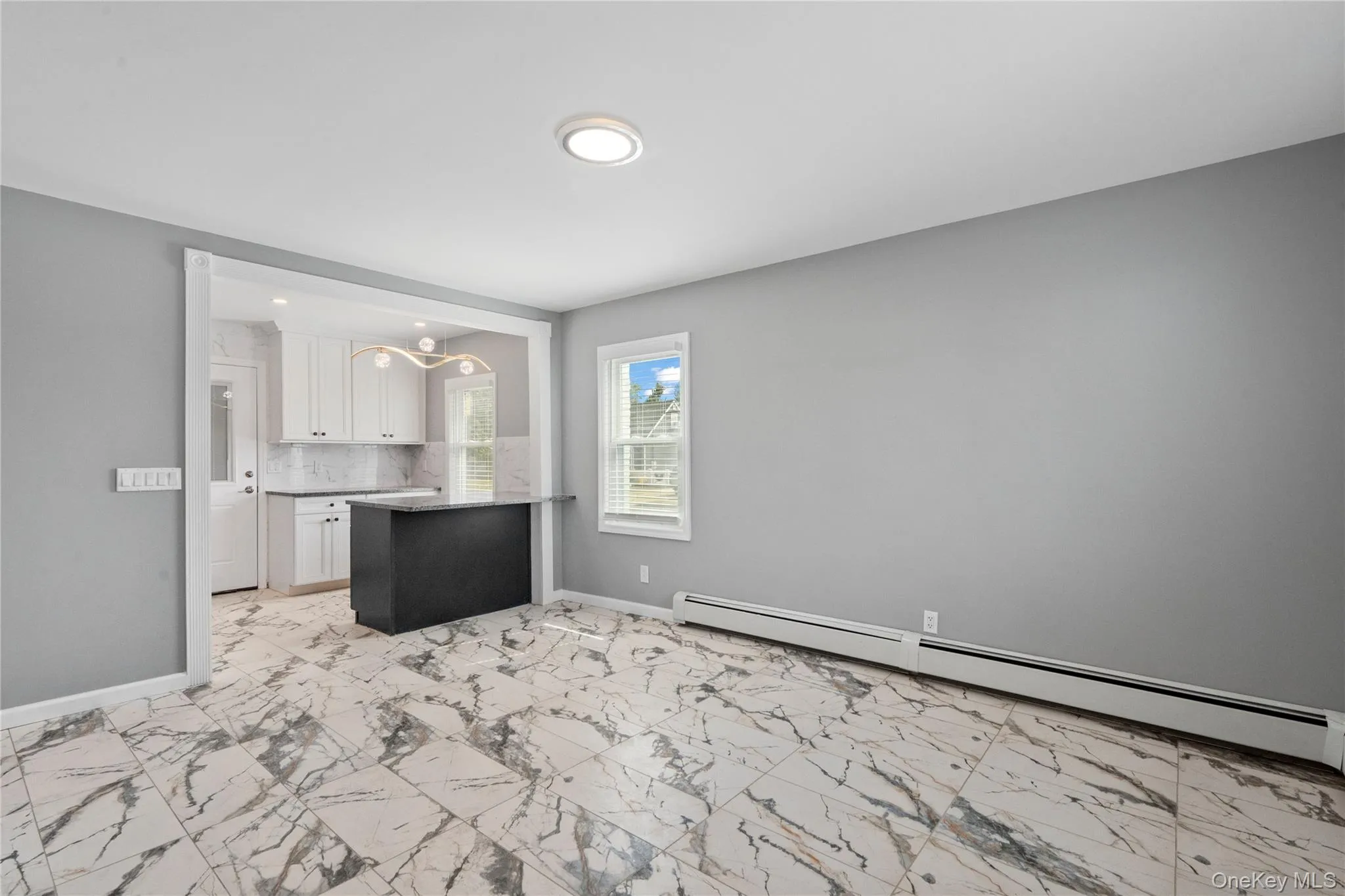 Unfurnished living room with a baseboard heating unit, light marble finish floors, and a chandelier Unfurnished living room with a baseboard heating unit, light marble finish floors, and a chandelier