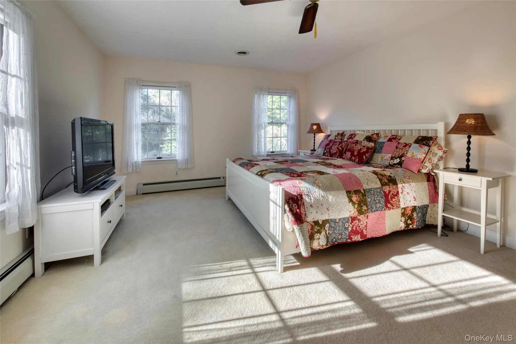 Bedroom featuring light colored carpet, a baseboard heating unit, and a ceiling fan Bedroom featuring light colored carpet, a baseboard heating unit, and a ceiling fan