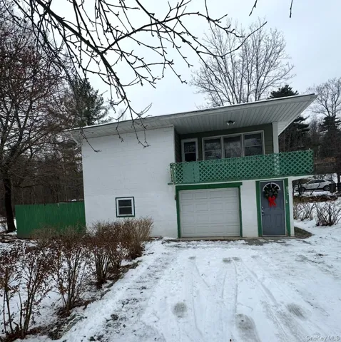 View of snowy exterior with a garage and a balcony