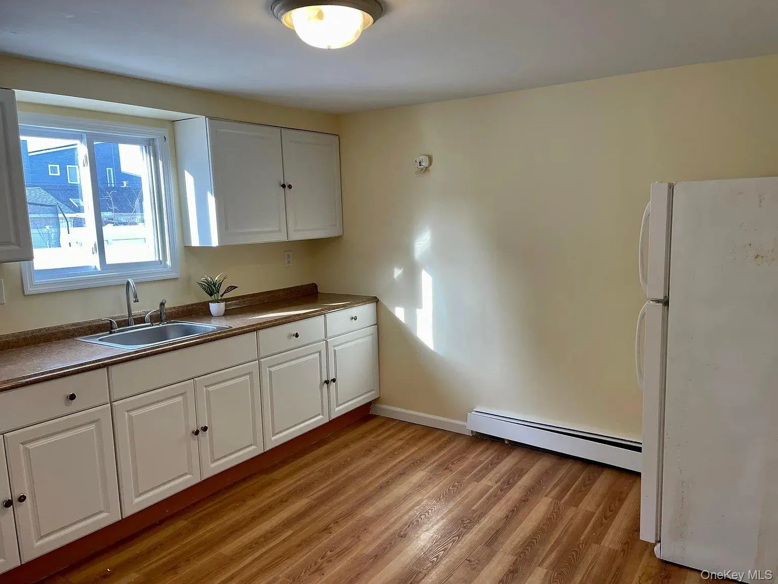 Kitchen with freestanding refrigerator, white cabinetry, light wood finished floors, and a baseboard heating unit Kitchen with freestanding refrigerator, white cabinetry, light wood finished floors, and a baseboard heating unit