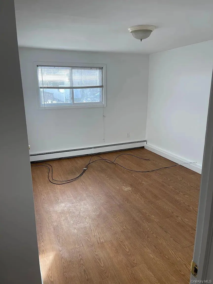 Unfurnished room featuring wood finished floors and a baseboard radiator Unfurnished room featuring wood finished floors and a baseboard radiator
