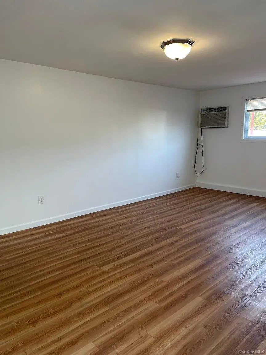 Unfurnished room with wood finished floors and an AC wall unit Unfurnished room with wood finished floors and an AC wall unit