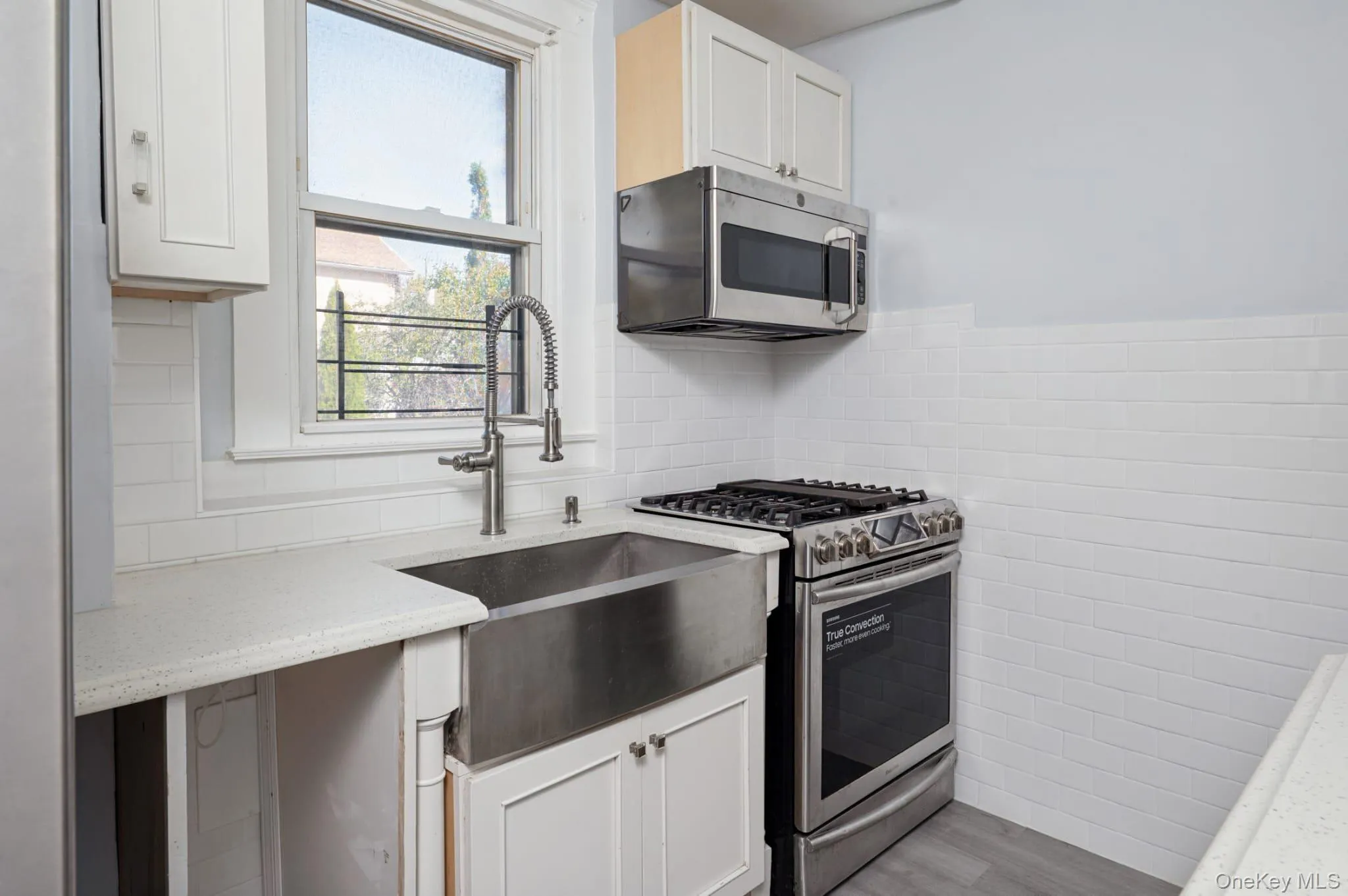 Kitchen with appliances with stainless steel finishes, tile walls, white cabinets, light wood-type flooring, and light stone counters Kitchen with appliances with stainless steel finishes, tile walls, white cabinets, light wood-type flooring, and light stone counters