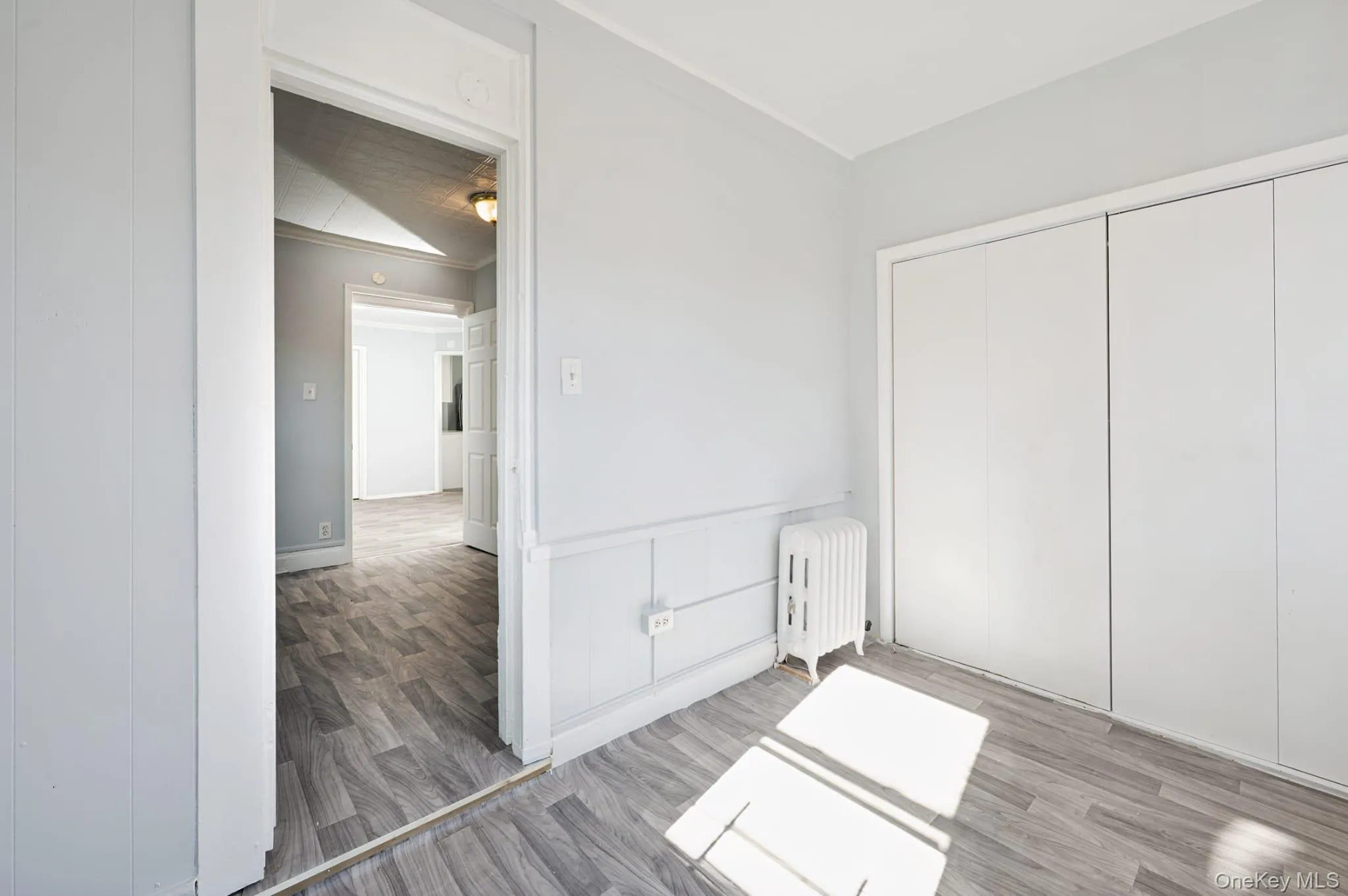 Unfurnished bedroom featuring radiator, light wood-type flooring, a closet, and wainscoting Unfurnished bedroom featuring radiator, light wood-type flooring, a closet, and wainscoting