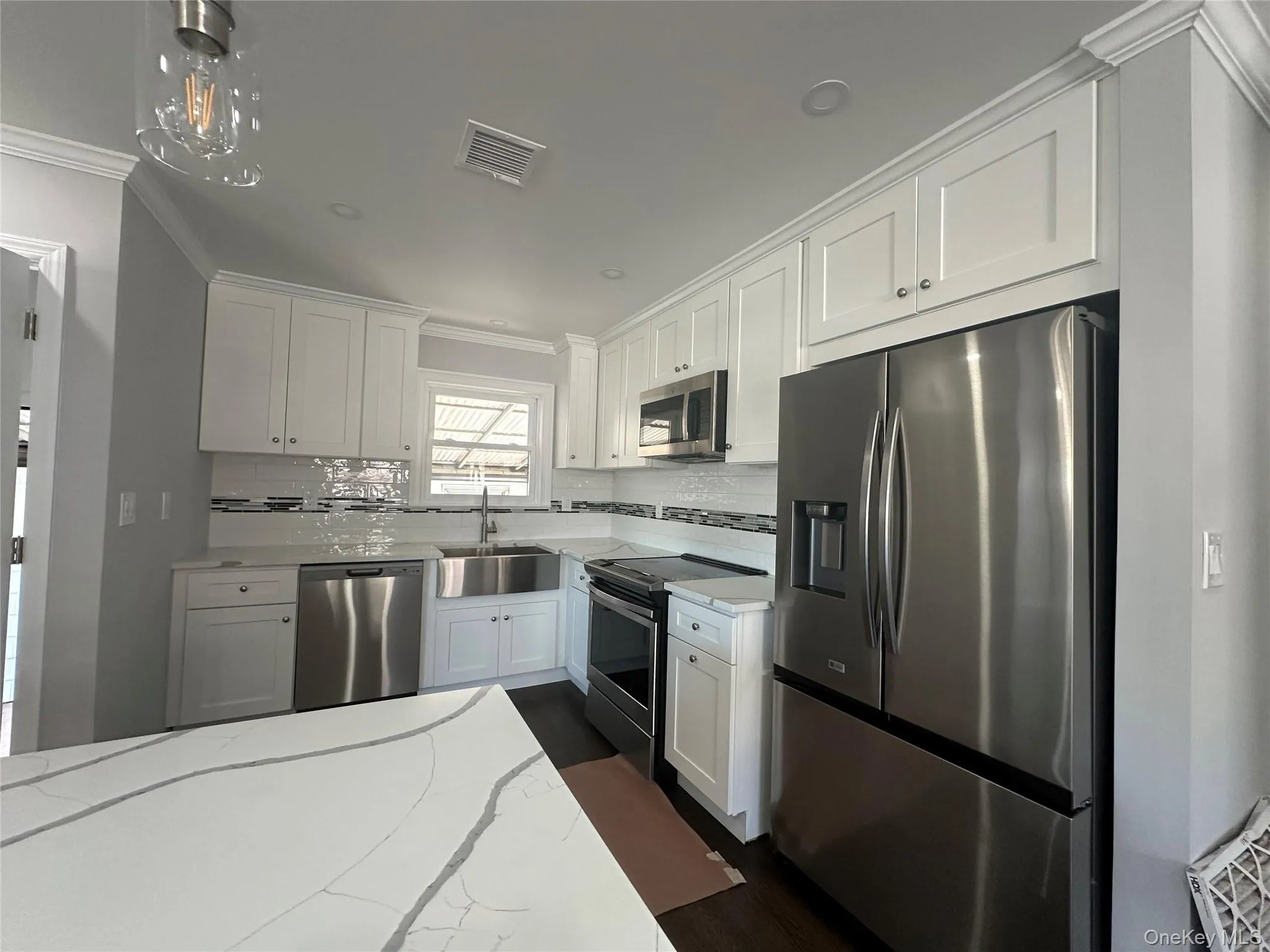 Kitchen with ornamental molding, stainless steel appliances, white cabinetry, light stone countertops, and tasteful backsplash Kitchen with ornamental molding, stainless steel appliances, white cabinetry, light stone countertops, and tasteful backsplash