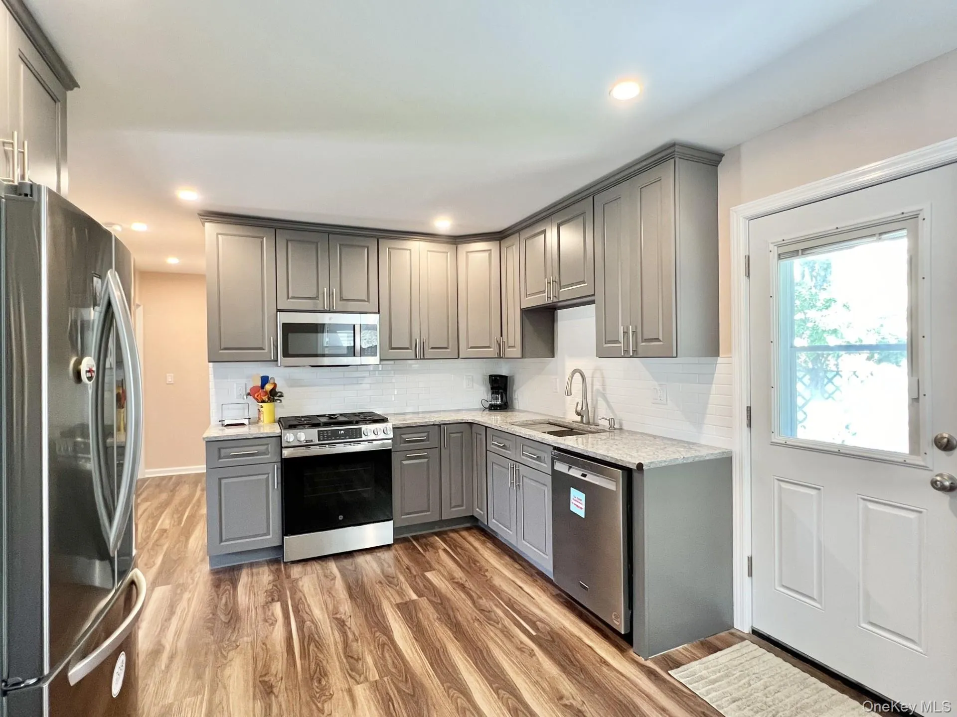 Kitchen with gray cabinetry, stainless steel appliances, light wood-style flooring, tasteful backsplash, and light stone countertops Kitchen with gray cabinetry, stainless steel appliances, light wood-style flooring, tasteful backsplash, and light stone countertops