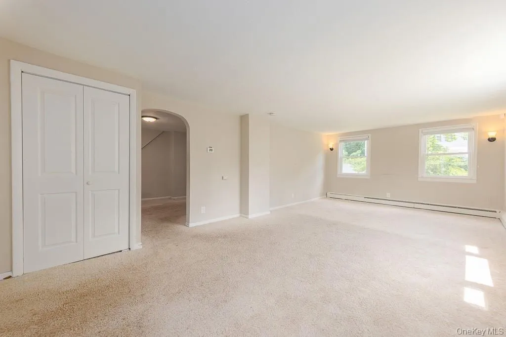 Spare room featuring arched walkways, light colored carpet, and a baseboard radiator Spare room featuring arched walkways, light colored carpet, and a baseboard radiator