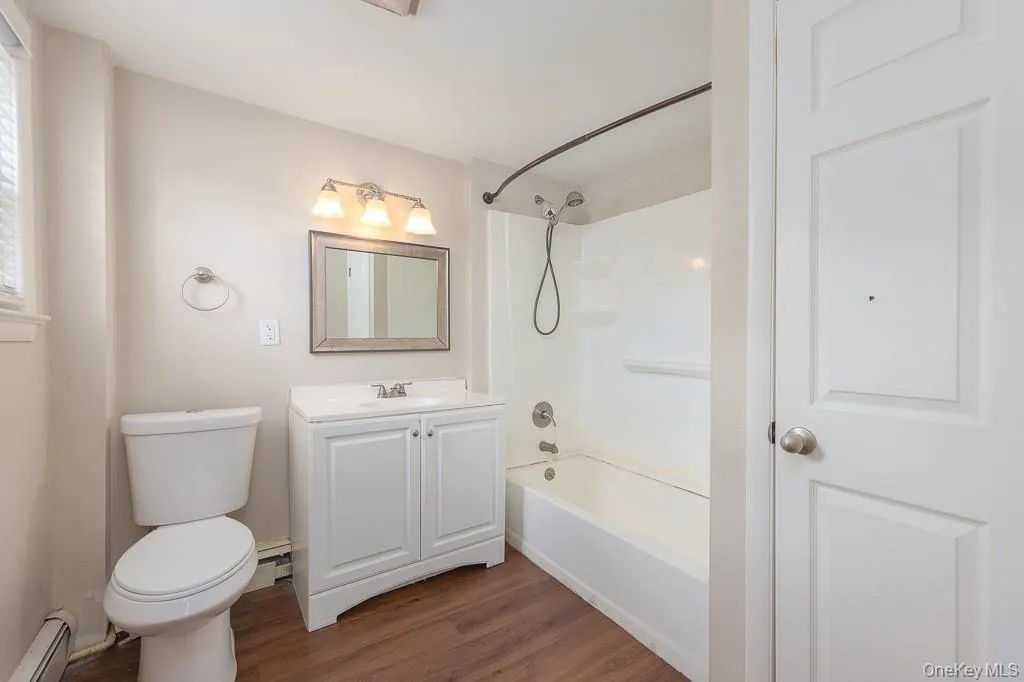 Bathroom with vanity, dark wood-type flooring, shower / tub combination, baseboard heating, and a baseboard heating unit Bathroom with vanity, dark wood-type flooring, shower / tub combination, baseboard heating, and a baseboard heating unit