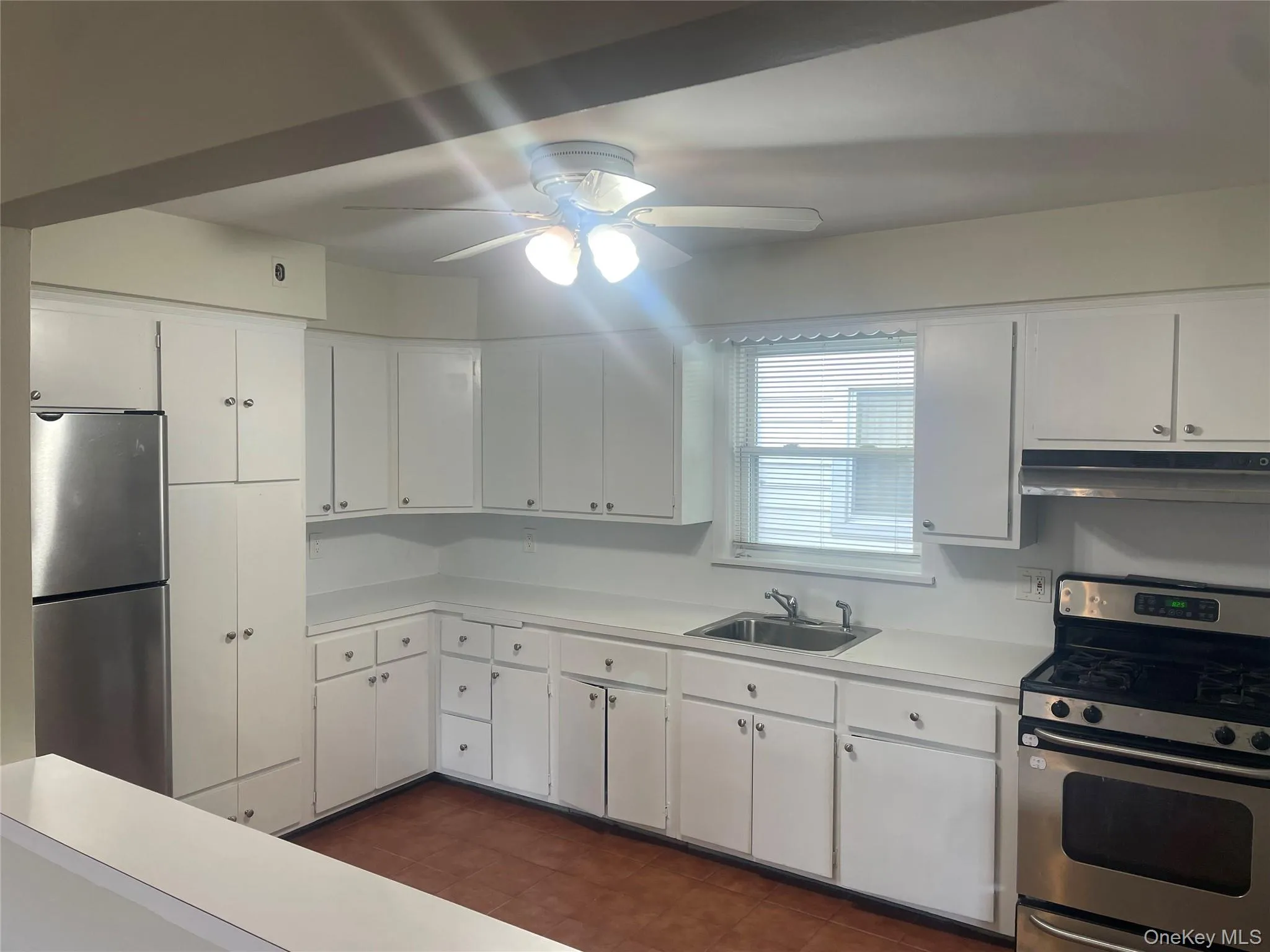 Kitchen featuring appliances with stainless steel finishes, light countertops, white cabinets, under cabinet range hood, and ceiling fan Kitchen featuring appliances with stainless steel finishes, light countertops, white cabinets, under cabinet range hood, and ceiling fan