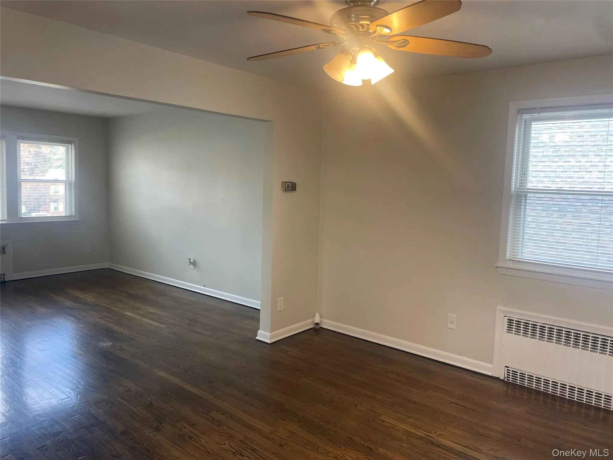 Unfurnished room with dark wood-style floors, a ceiling fan, and radiator heating unit Unfurnished room with dark wood-style floors, a ceiling fan, and radiator heating unit