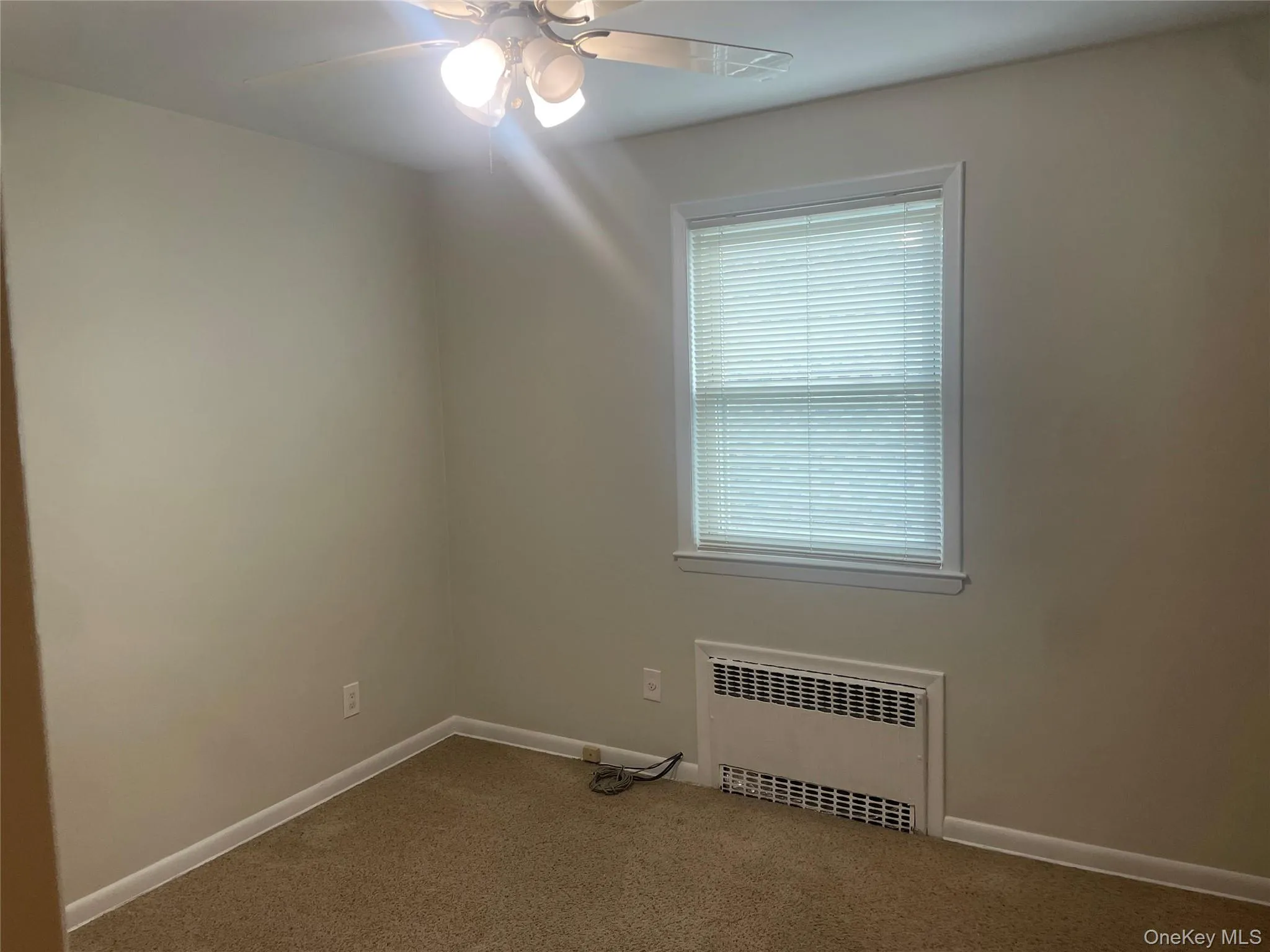 Spare room with carpet floors, radiator heating unit, and ceiling fan Spare room with carpet floors, radiator heating unit, and ceiling fan
