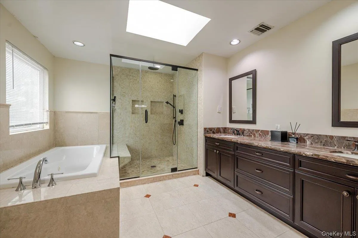 Full bath with a bath, a skylight, double vanity, a shower stall, and light tile patterned floors Full bath with a bath, a skylight, double vanity, a shower stall, and light tile patterned floors
