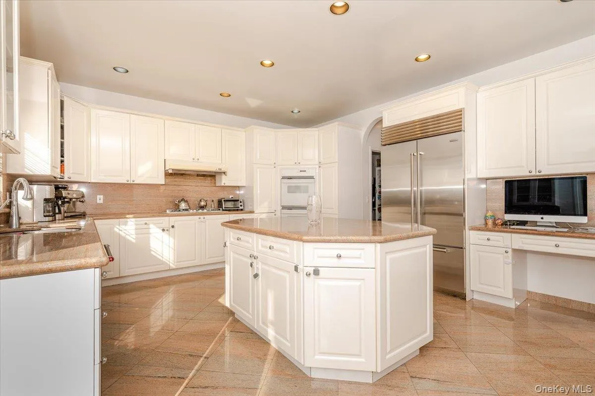 Kitchen featuring backsplash, stainless steel built in fridge, white cabinets, recessed lighting, and light stone counters Kitchen featuring backsplash, stainless steel built in fridge, white cabinets, recessed lighting, and light stone counters
