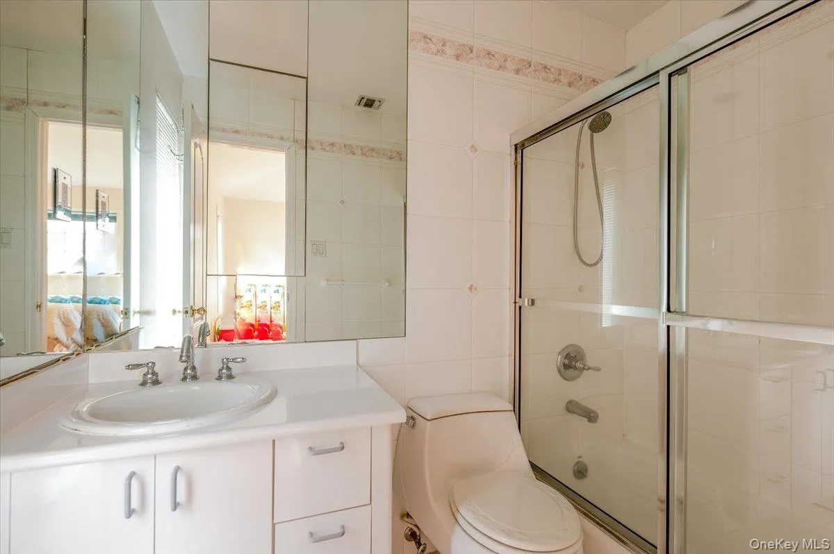 Full bathroom featuring tile walls, vanity, and combined bath / shower with glass door Full bathroom featuring tile walls, vanity, and combined bath / shower with glass door