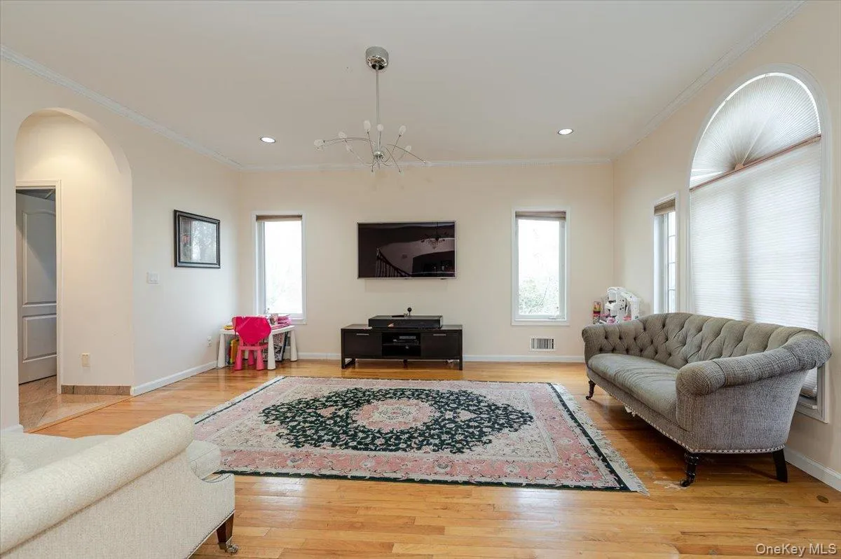 Living room with light wood-style flooring, crown molding, arched walkways, recessed lighting, and a chandelier Living room with light wood-style flooring, crown molding, arched walkways, recessed lighting, and a chandelier