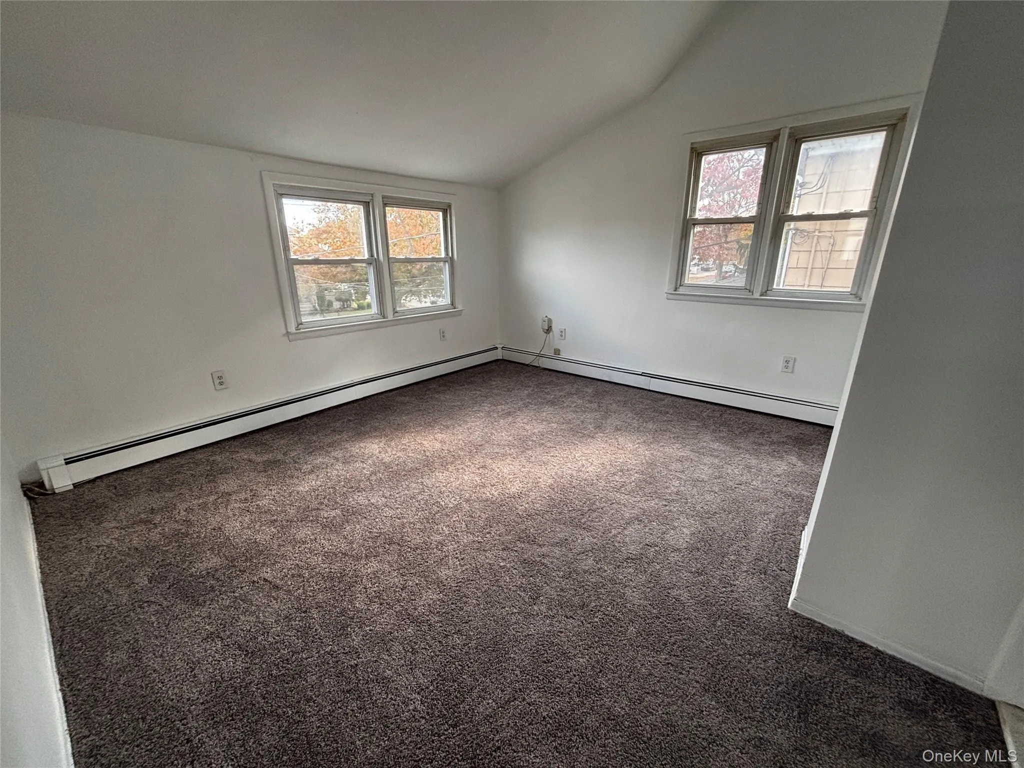 Unfurnished room with lofted ceiling, dark carpet, and a baseboard radiator Unfurnished room with lofted ceiling, dark carpet, and a baseboard radiator