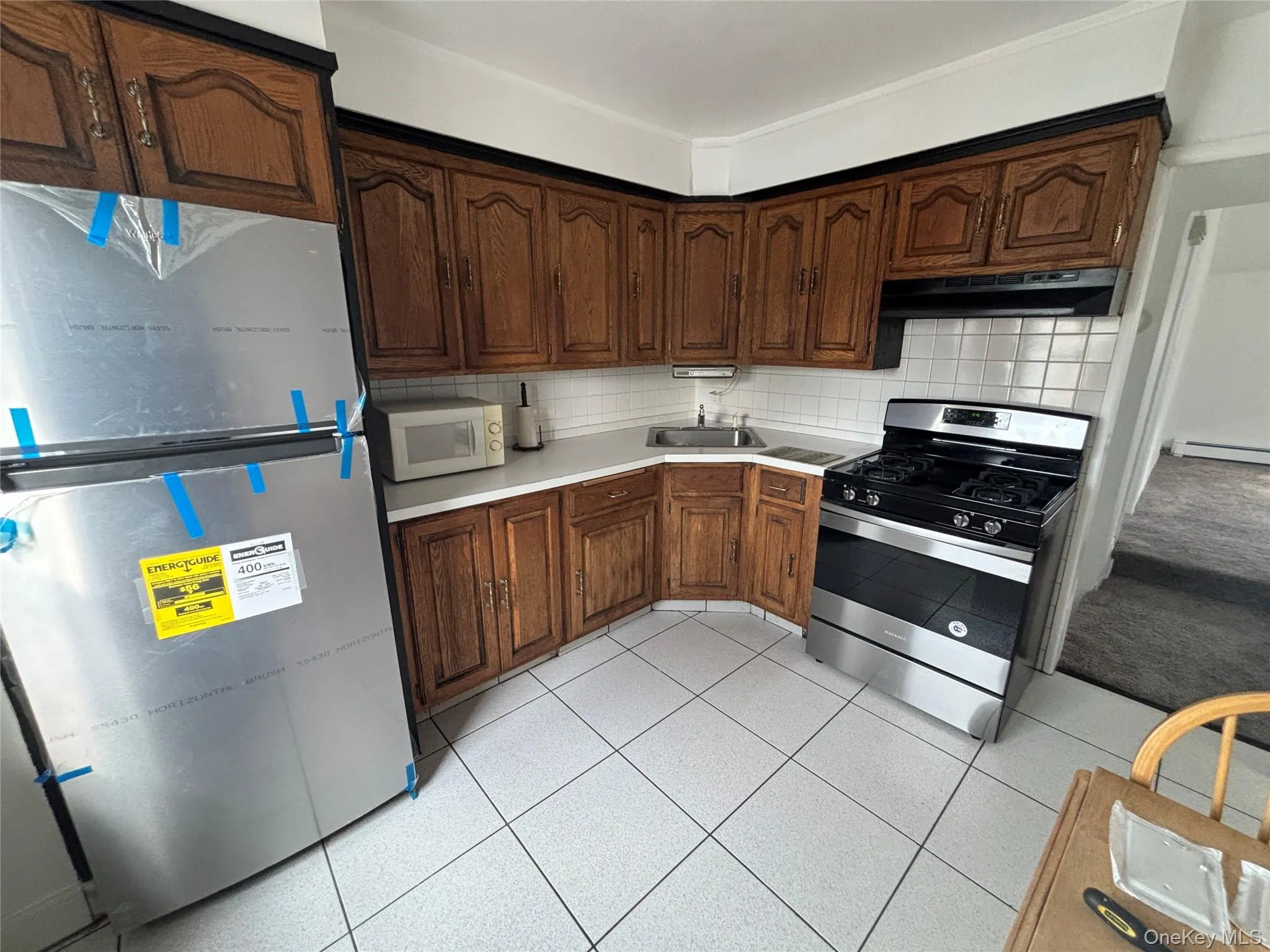 Kitchen with fridge, gas stove, light tile patterned flooring, decorative backsplash, and light countertops Kitchen with fridge, gas stove, light tile patterned flooring, decorative backsplash, and light countertops