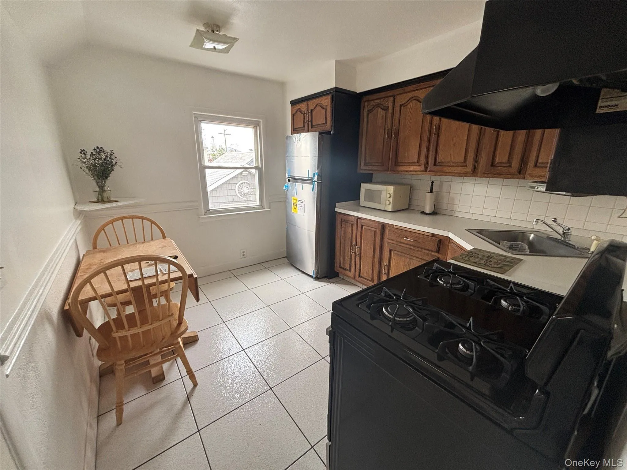 Kitchen featuring extractor fan, black gas range oven, light countertops, light tile patterned flooring, and decorative backsplash Kitchen featuring extractor fan, black gas range oven, light countertops, light tile patterned flooring, and decorative backsplash