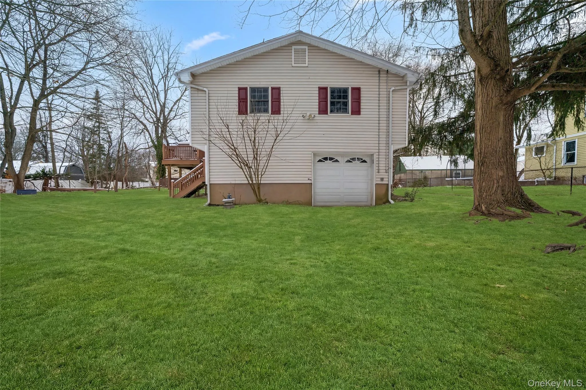 Back of property featuring stairway, a wooden deck, a lawn, and an attached garage Back of property featuring stairway, a wooden deck, a lawn, and an attached garage