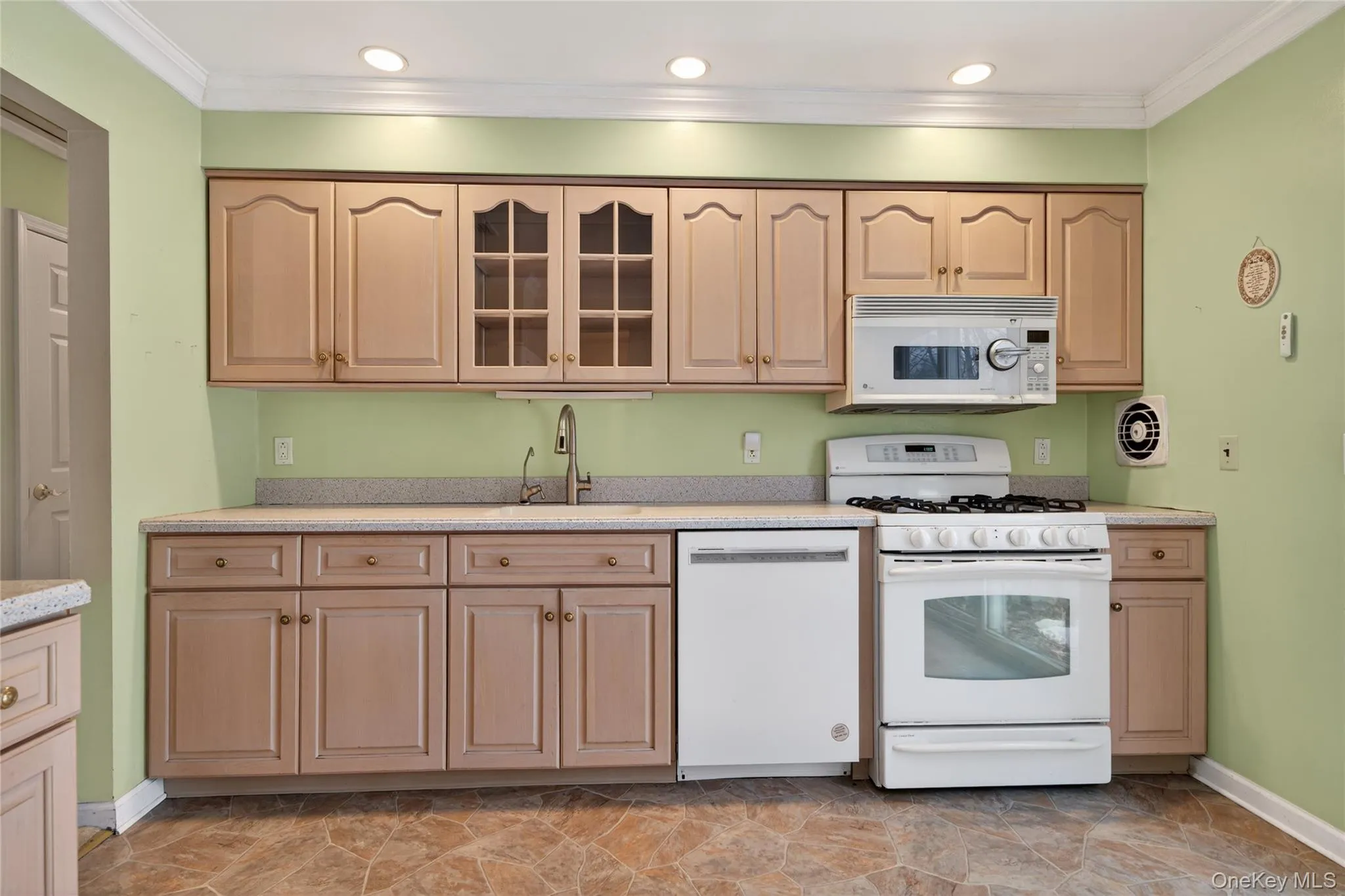 Kitchen with white appliances, glass insert cabinets, light brown cabinets, crown molding, and light stone counters Kitchen with white appliances, glass insert cabinets, light brown cabinets, crown molding, and light stone counters