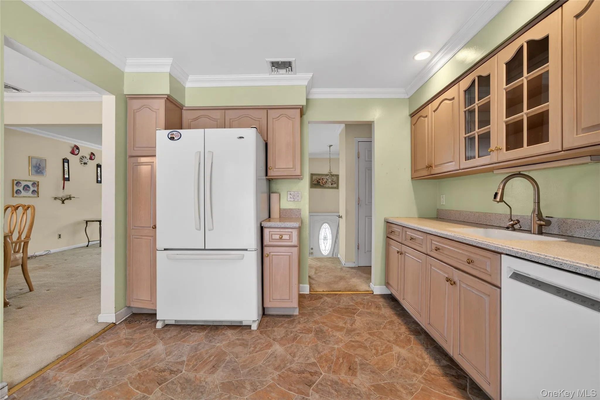 Kitchen with white appliances, glass insert cabinets, ornamental molding, light stone finish floors, and light stone countertops Kitchen with white appliances, glass insert cabinets, ornamental molding, light stone finish floors, and light stone countertops