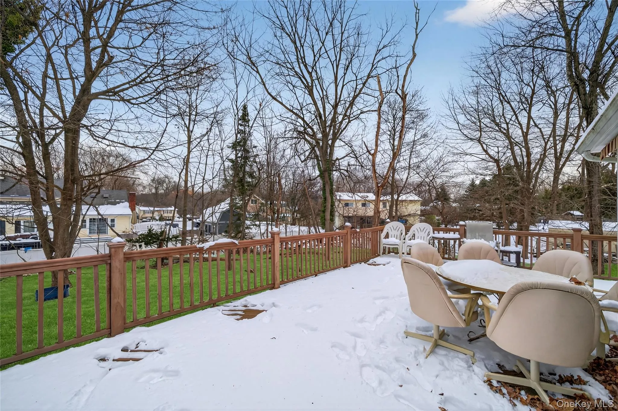 Yard covered in snow with a deck, outdoor dining space, a lawn, and a residential view Yard covered in snow with a deck, outdoor dining space, a lawn, and a residential view
