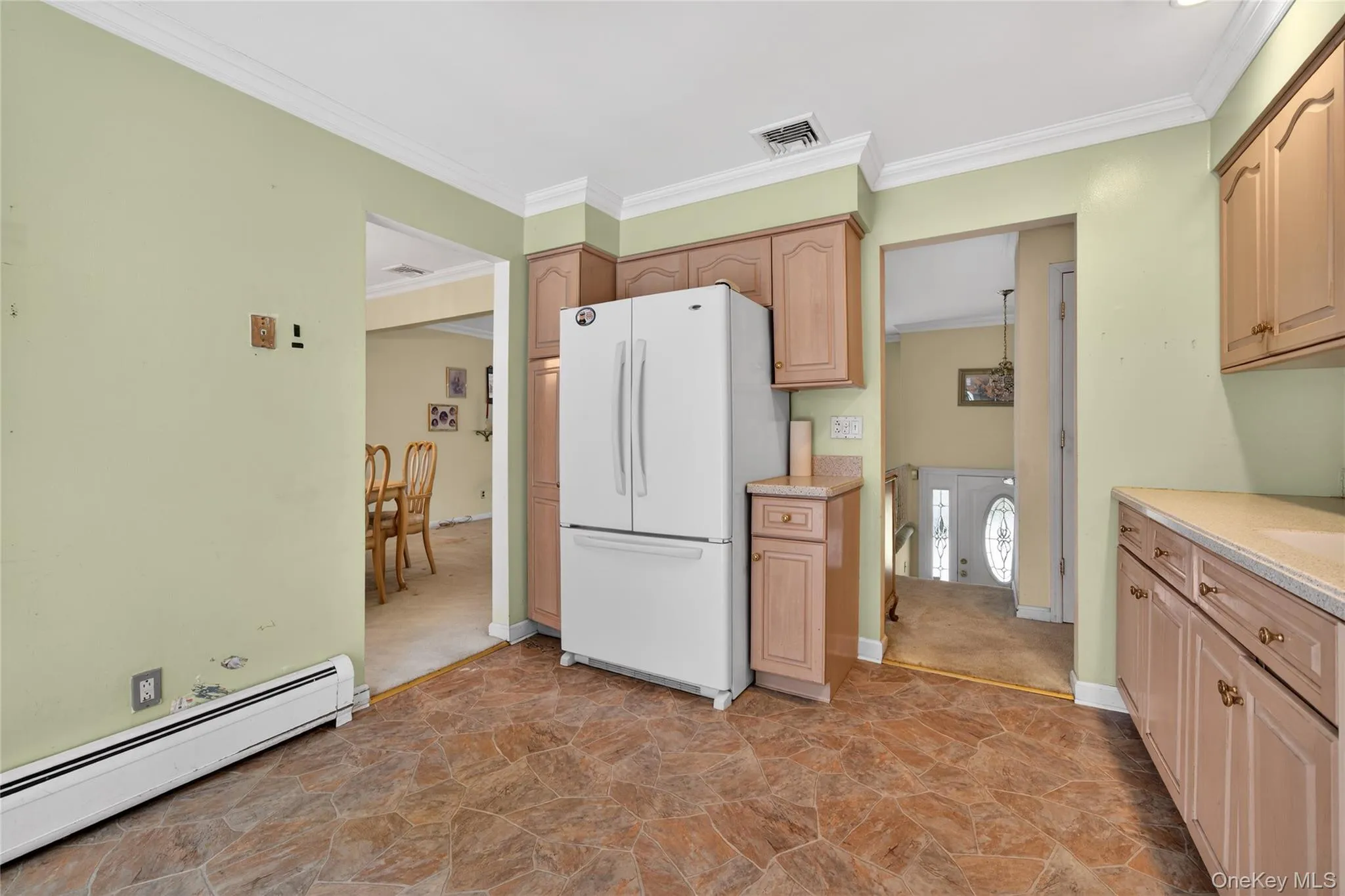 Kitchen featuring baseboard heating, freestanding refrigerator, crown molding, and light stone finish floors Kitchen featuring baseboard heating, freestanding refrigerator, crown molding, and light stone finish floors