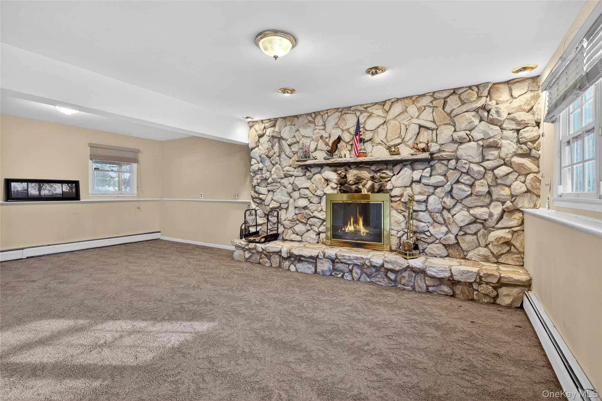 Unfurnished living room featuring a baseboard radiator, a stone fireplace, and carpet Unfurnished living room featuring a baseboard radiator, a stone fireplace, and carpet