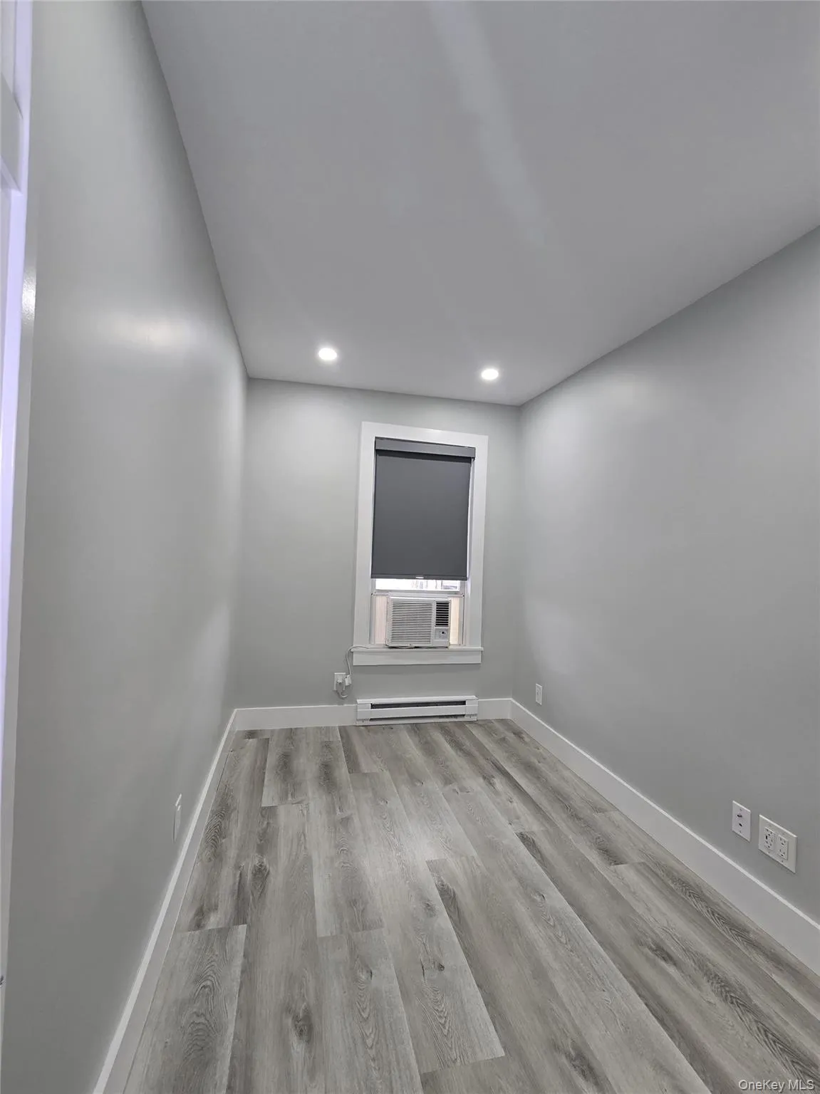 Empty room featuring light wood-type flooring, recessed lighting, a baseboard radiator, and cooling unit Empty room featuring light wood-type flooring, recessed lighting, a baseboard radiator, and cooling unit