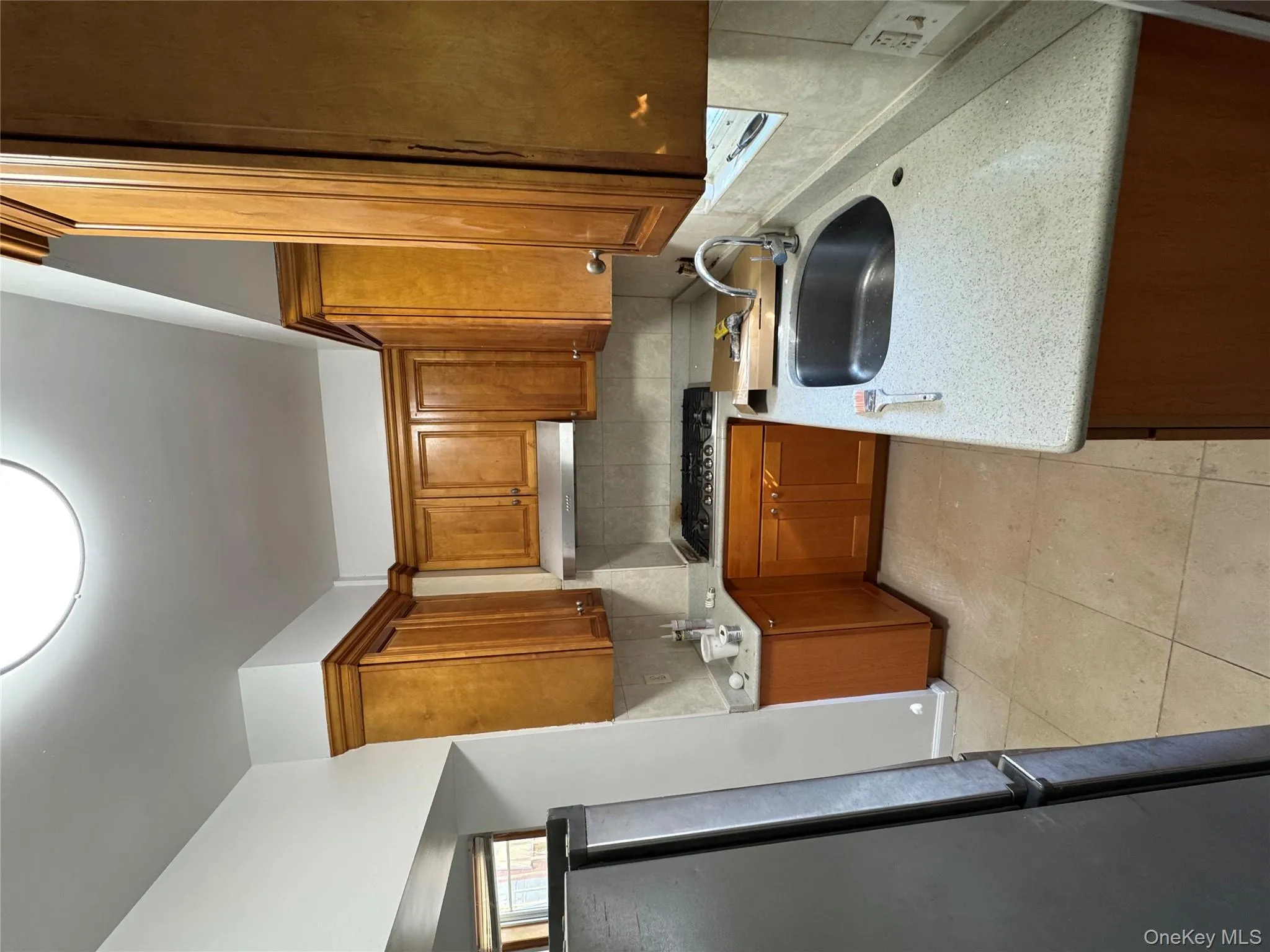 Kitchen featuring decorative backsplash, fridge, brown cabinets, light tile patterned floors, and light stone countertops Kitchen featuring decorative backsplash, fridge, brown cabinets, light tile patterned floors, and light stone countertops