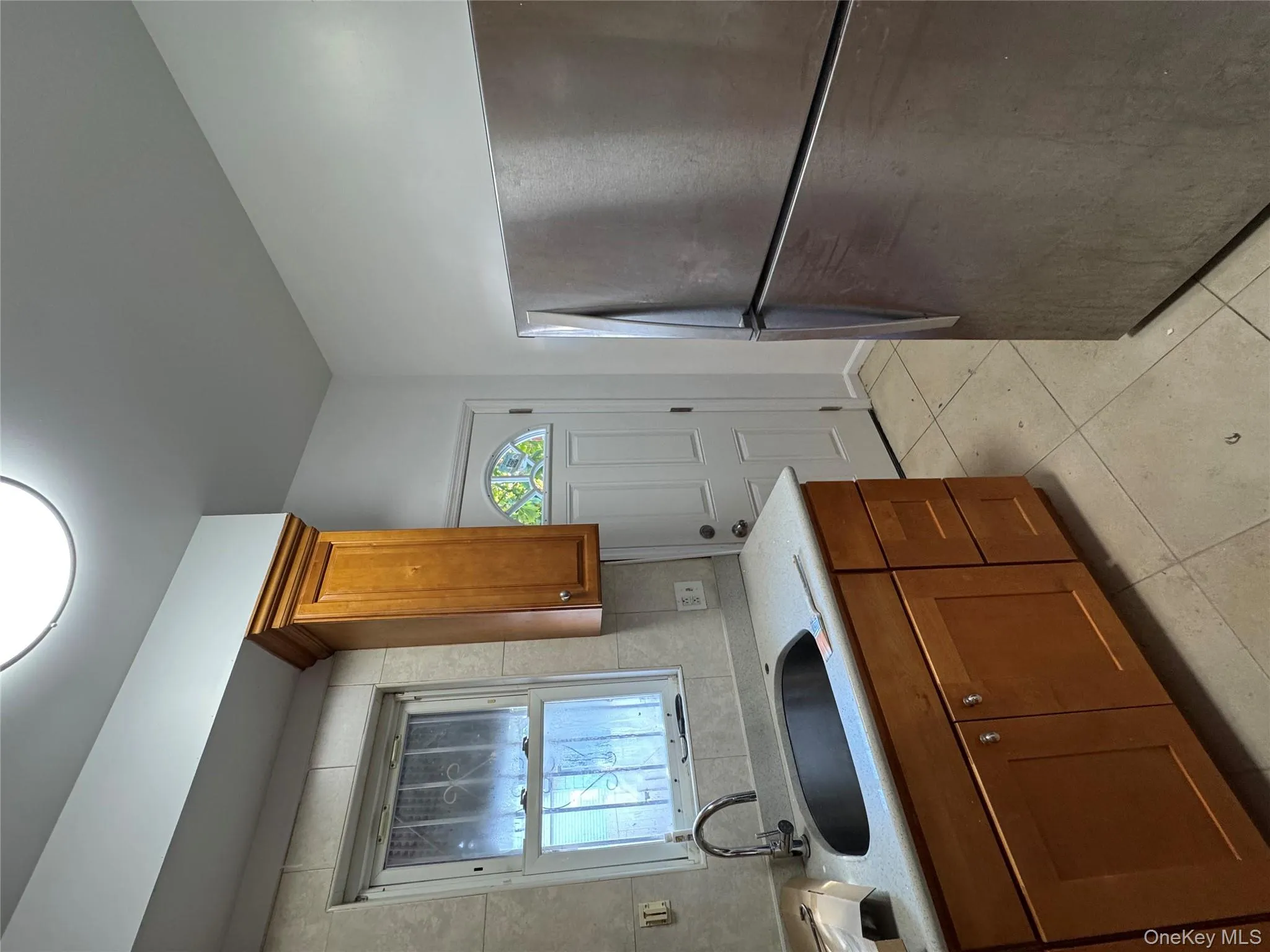 Kitchen featuring fridge, brown cabinetry, light stone countertops, and light tile patterned floors Kitchen featuring fridge, brown cabinetry, light stone countertops, and light tile patterned floors