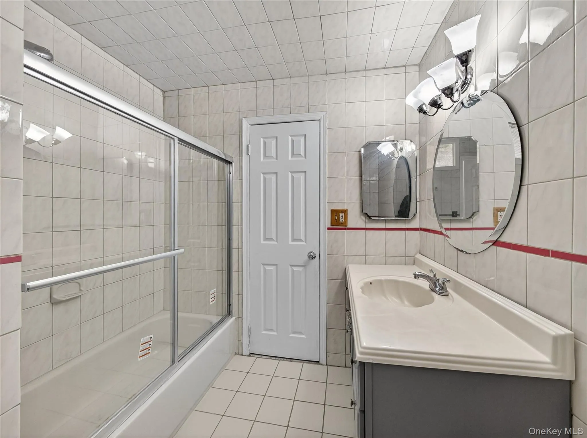 Bathroom featuring tile walls, enclosed tub / shower combo, vanity, and light tile patterned floors Bathroom featuring tile walls, enclosed tub / shower combo, vanity, and light tile patterned floors