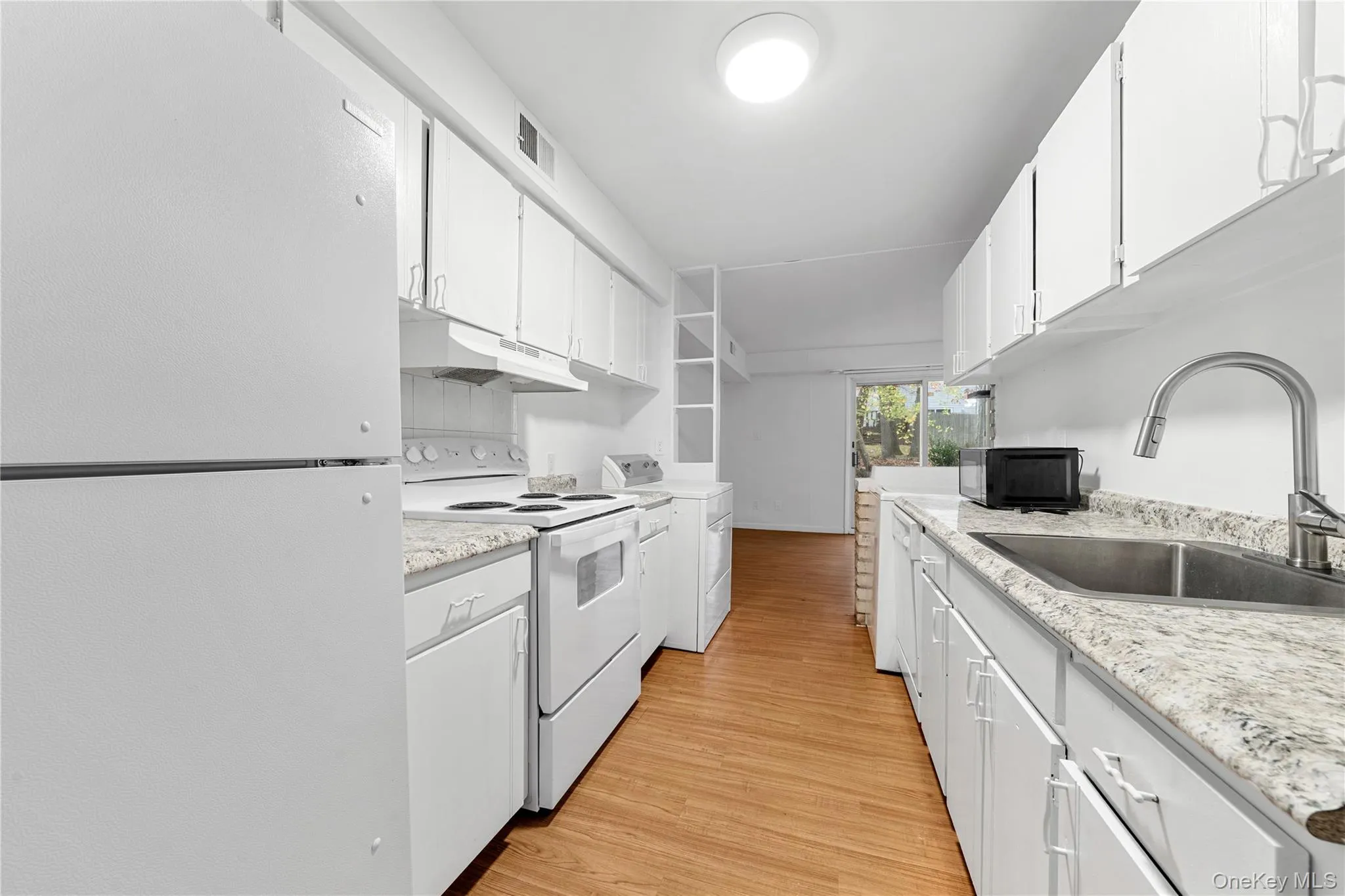 Kitchen featuring white appliances, light wood finished floors, white cabinets, and washer / dryer Kitchen featuring white appliances, light wood finished floors, white cabinets, and washer / dryer