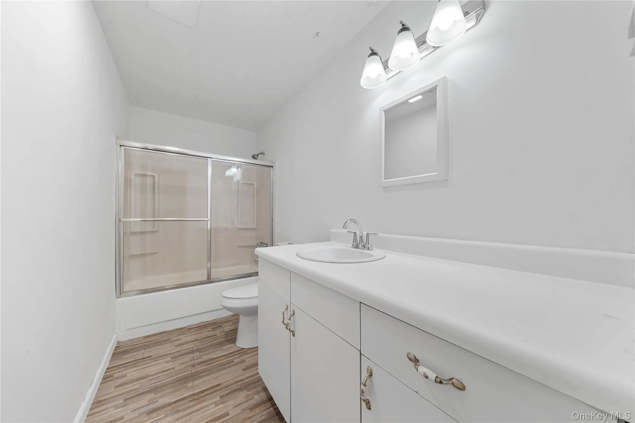 Bathroom with combined bath / shower with glass door, vanity, and light wood finished floors Bathroom with combined bath / shower with glass door, vanity, and light wood finished floors