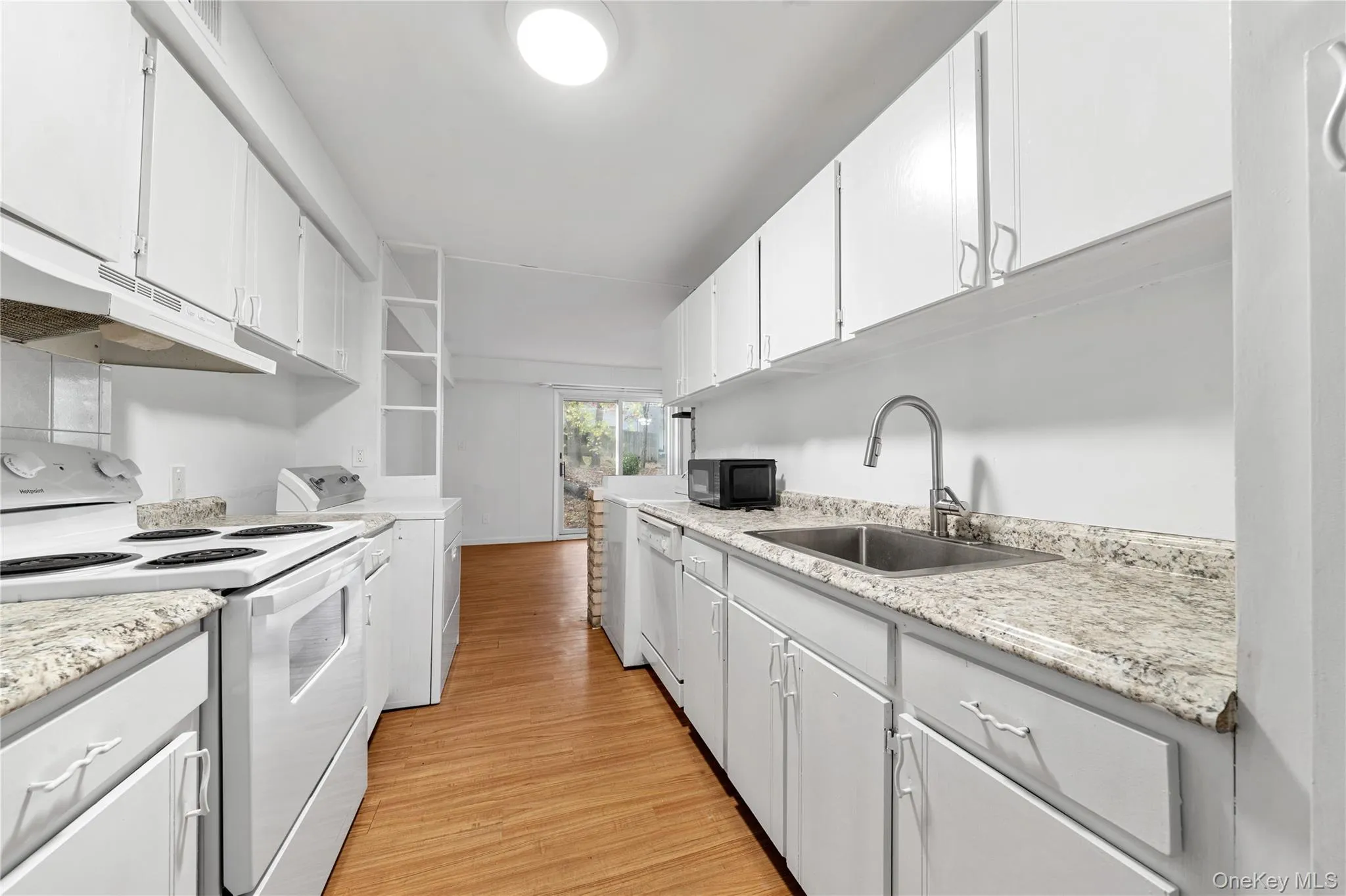 Kitchen with white appliances, open shelves, light wood-style flooring, white cabinets, and washer / dryer Kitchen with white appliances, open shelves, light wood-style flooring, white cabinets, and washer / dryer