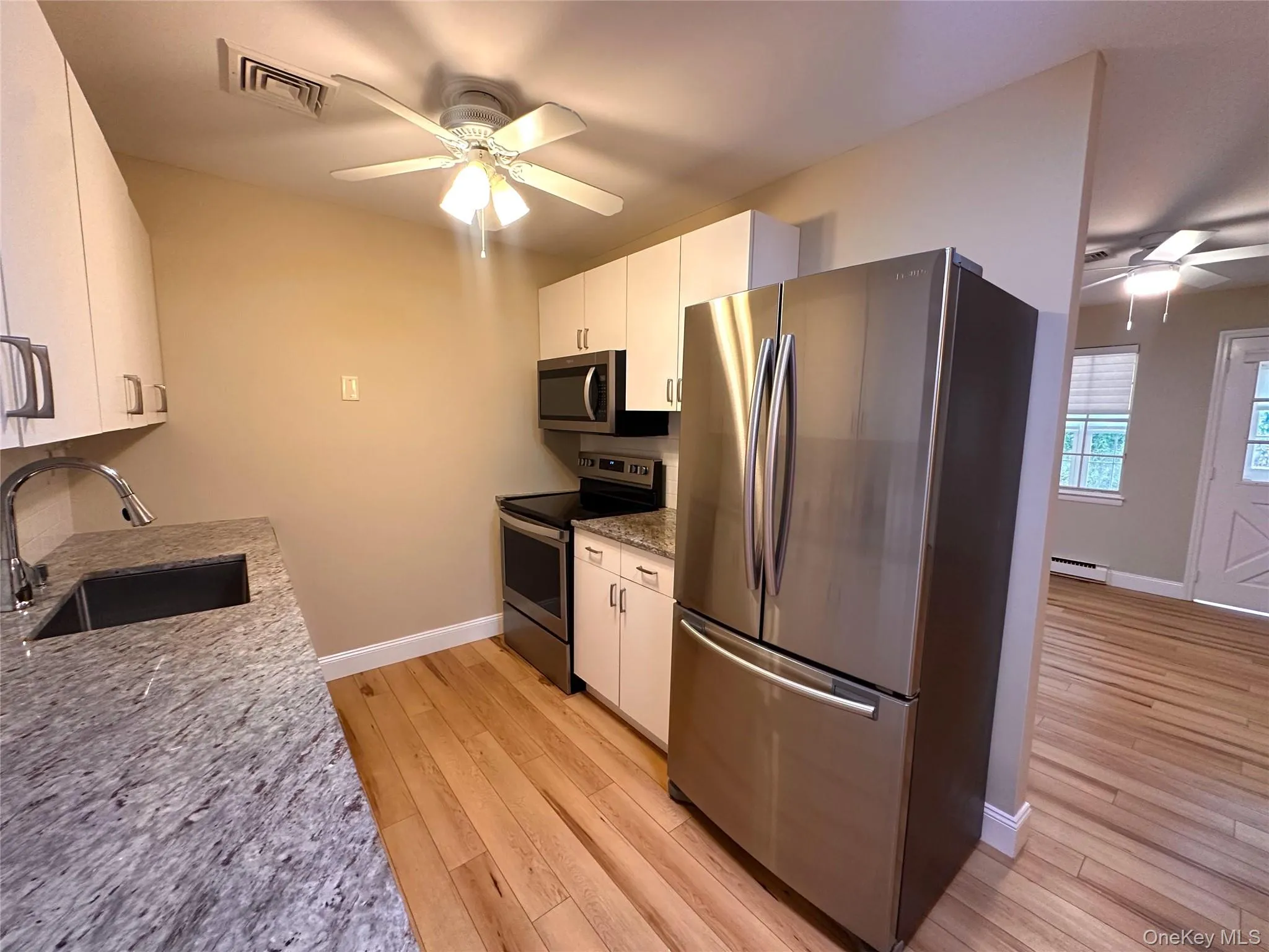 Kitchen featuring a ceiling fan, appliances with stainless steel finishes, light stone counters, and white cabinetry Kitchen featuring a ceiling fan, appliances with stainless steel finishes, light stone counters, and white cabinetry