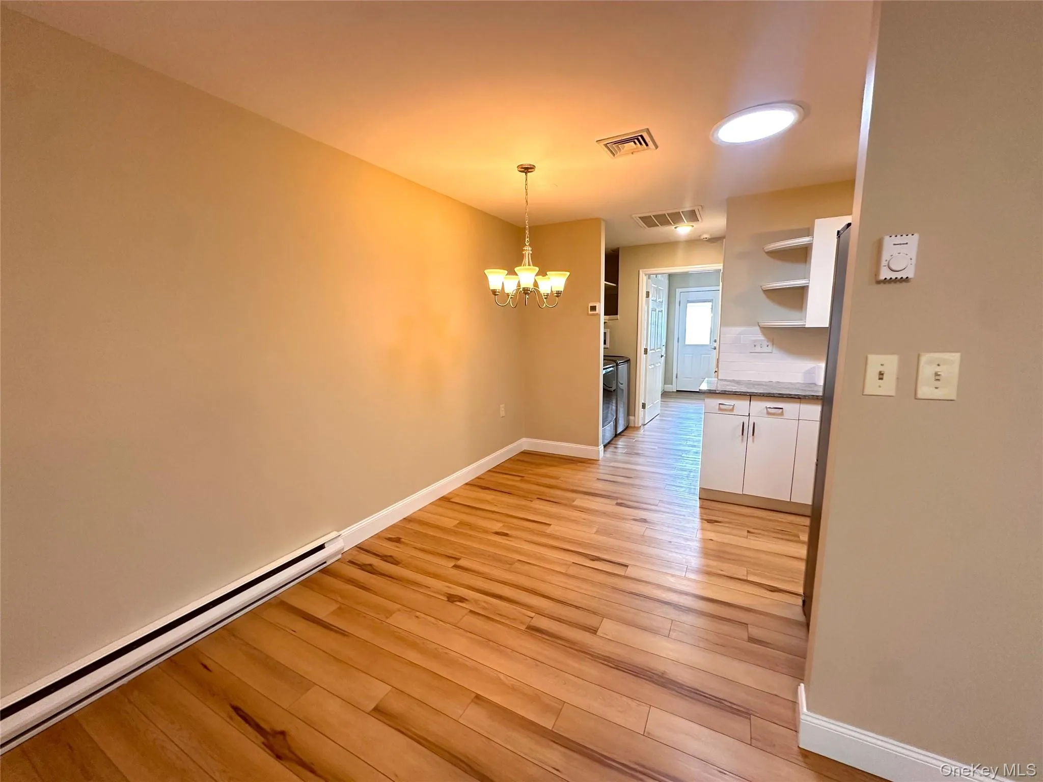 Unfurnished dining area with baseboard heating, a chandelier, and light wood finished floors Unfurnished dining area with baseboard heating, a chandelier, and light wood finished floors