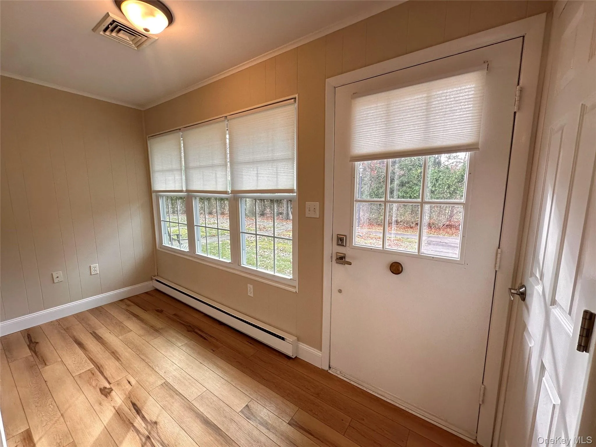 Doorway featuring a baseboard radiator, ornamental molding, healthy amount of natural light, wood-type flooring, and wood walls Doorway featuring a baseboard radiator, ornamental molding, healthy amount of natural light, wood-type flooring, and wood walls