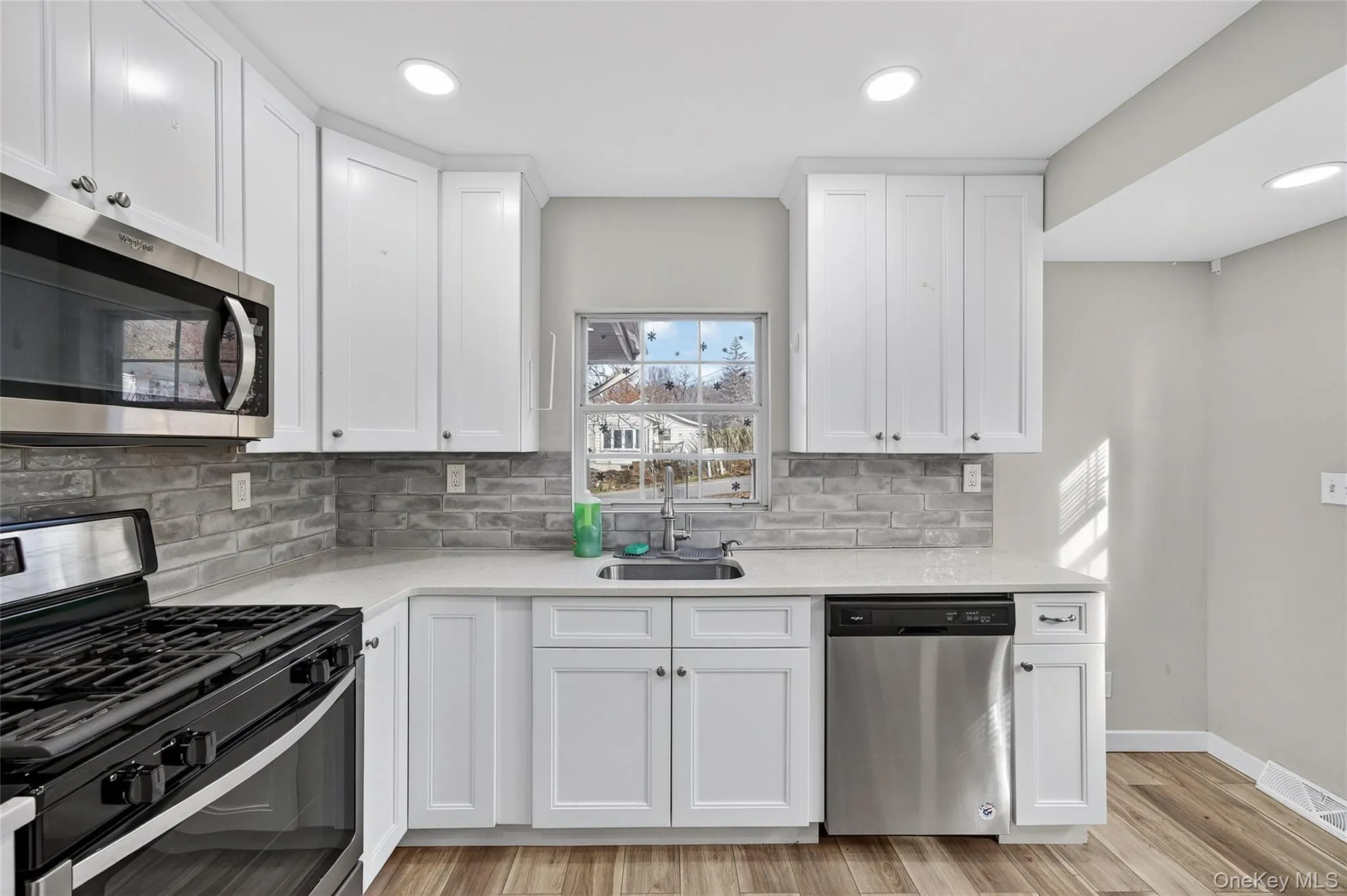 Kitchen featuring stainless steel appliances, white cabinets, tasteful backsplash, light wood-type flooring, and recessed lighting Kitchen featuring stainless steel appliances, white cabinets, tasteful backsplash, light wood-type flooring, and recessed lighting
