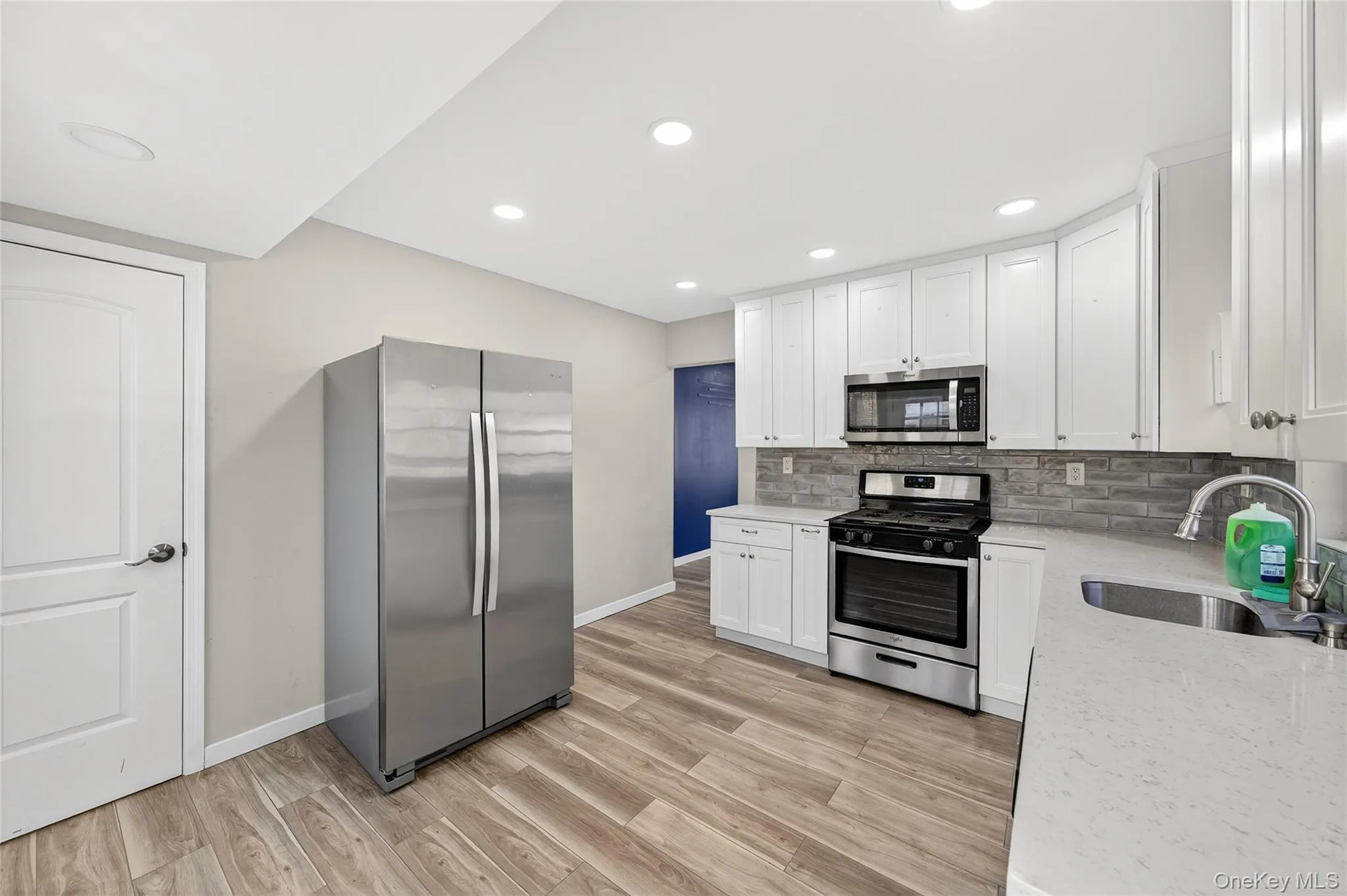 Kitchen with appliances with stainless steel finishes, light stone counters, white cabinets, tasteful backsplash, and light wood-style flooring Kitchen with appliances with stainless steel finishes, light stone counters, white cabinets, tasteful backsplash, and light wood-style flooring