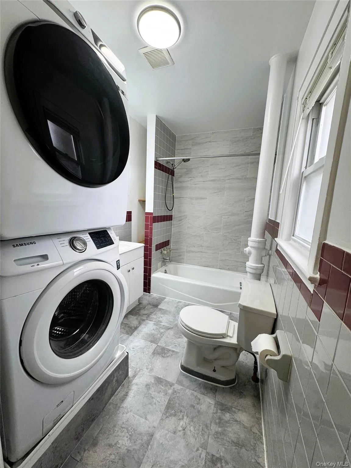 Bathroom featuring shower / tub combination, stacked washing machine and dryer, and tile walls Bathroom featuring shower / tub combination, stacked washing machine and dryer, and tile walls