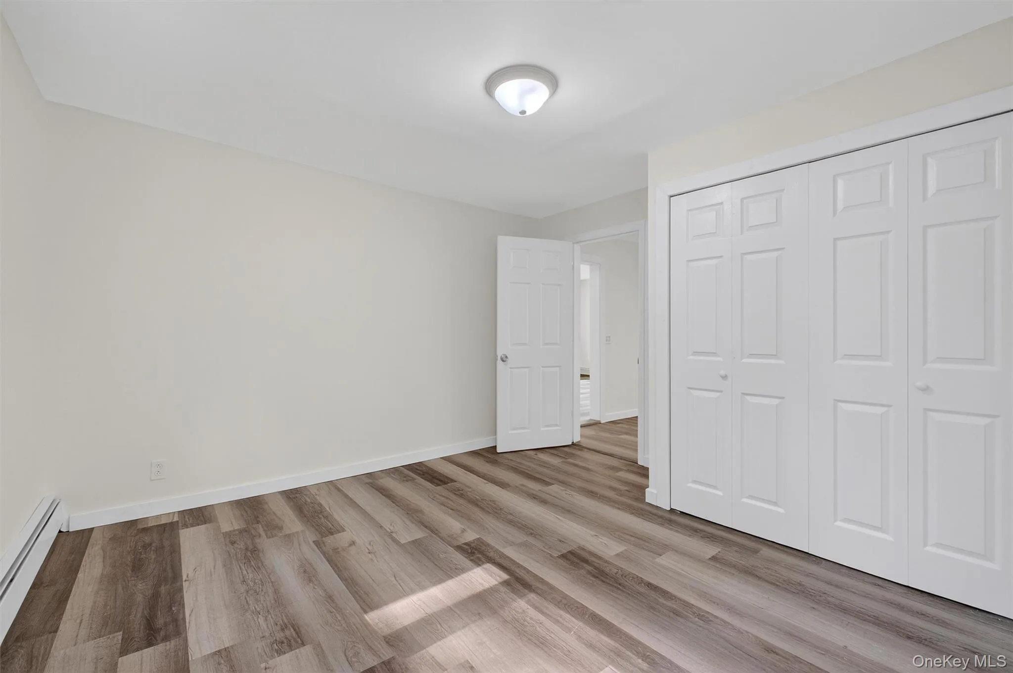 Unfurnished bedroom featuring a baseboard heating unit, light wood-style flooring, and a closet Unfurnished bedroom featuring a baseboard heating unit, light wood-style flooring, and a closet