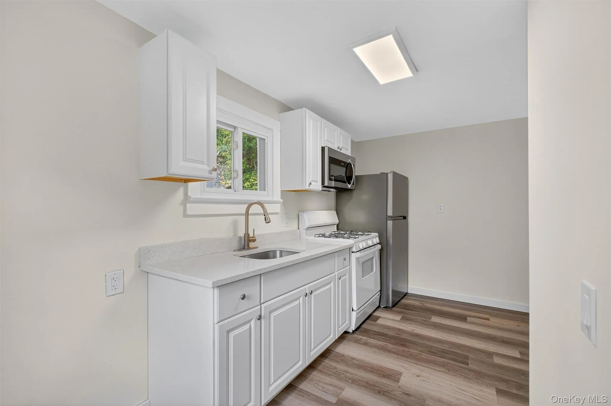 Kitchen featuring white gas range oven, white cabinetry, stainless steel microwave, light wood-style flooring, and light stone countertops Kitchen featuring white gas range oven, white cabinetry, stainless steel microwave, light wood-style flooring, and light stone countertops