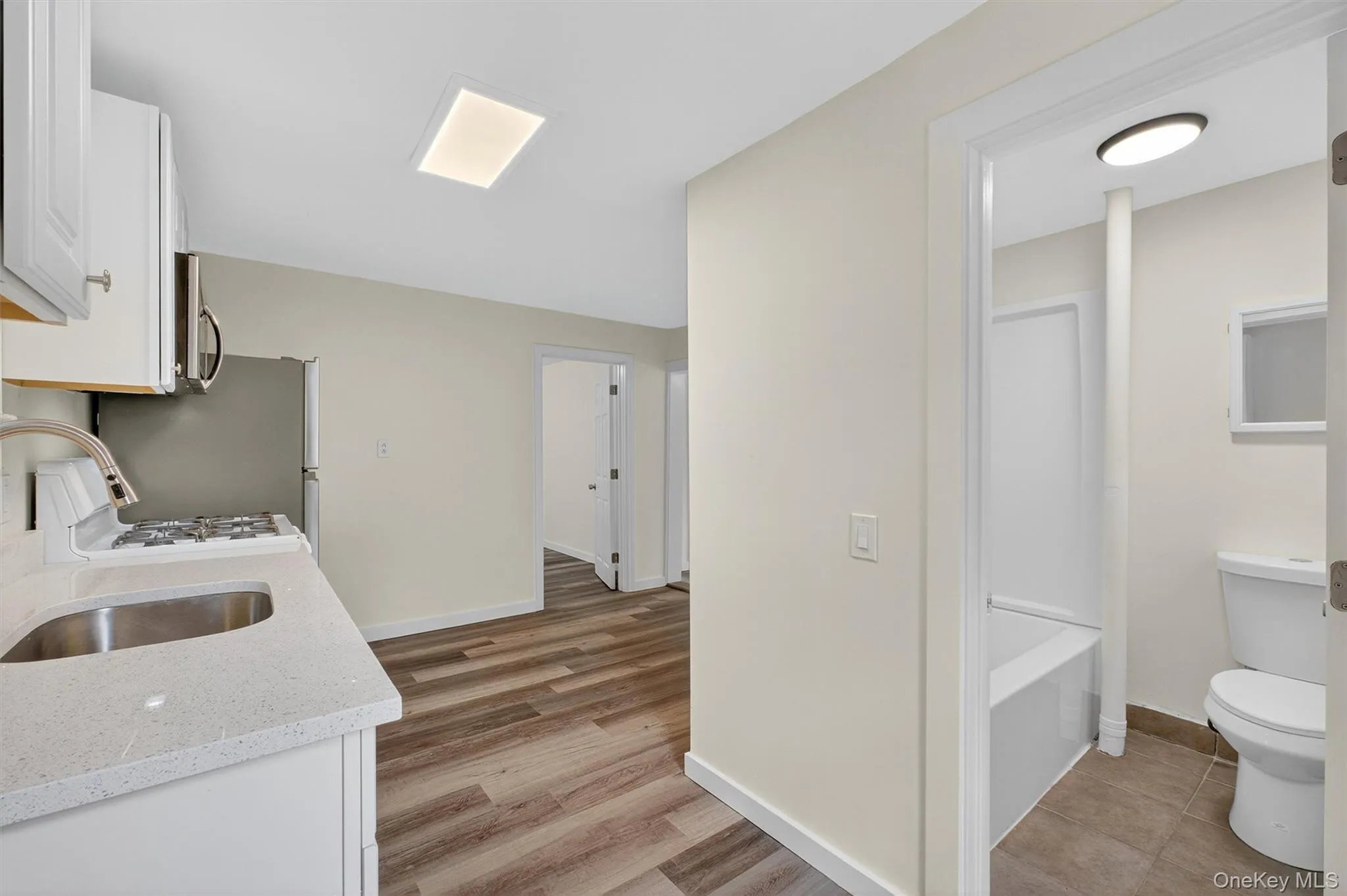 Kitchen with white cabinets, light stone counters, white gas range, light wood-style flooring, and stainless steel microwave Kitchen with white cabinets, light stone counters, white gas range, light wood-style flooring, and stainless steel microwave