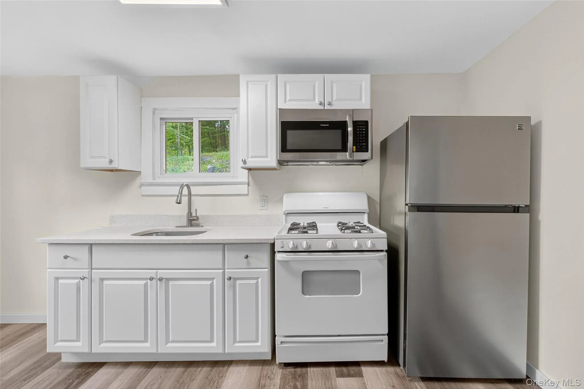 Kitchen with stainless steel appliances, white cabinets, light wood finished floors, and light stone countertops Kitchen with stainless steel appliances, white cabinets, light wood finished floors, and light stone countertops