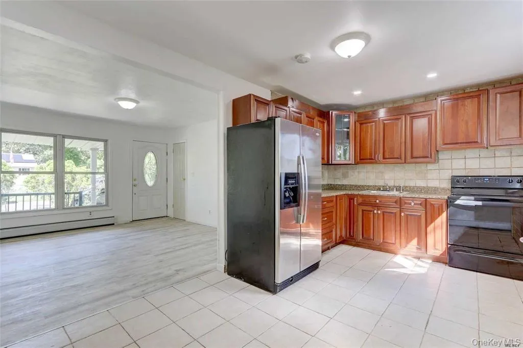 Kitchen featuring stainless steel fridge, electric range, brown cabinets, tasteful backsplash, and light tile patterned flooring Kitchen featuring stainless steel fridge, electric range, brown cabinets, tasteful backsplash, and light tile patterned flooring