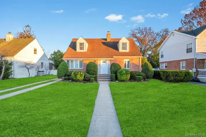 Cape cod house with a front lawn, a chimney, and brick siding