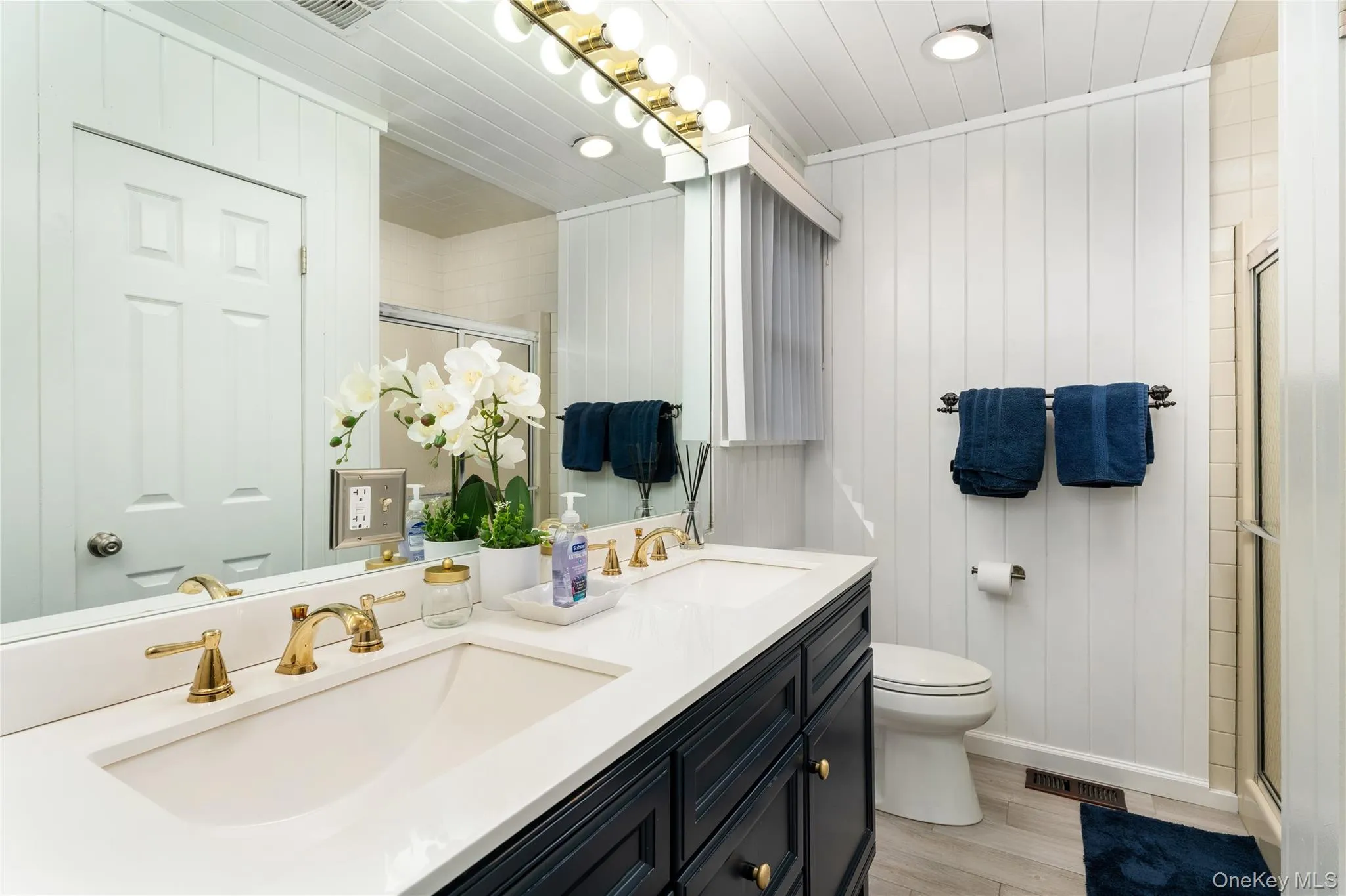 Bathroom featuring light wood-type flooring, double vanity, a stall shower, wood walls, and recessed lighting Bathroom featuring light wood-type flooring, double vanity, a stall shower, wood walls, and recessed lighting