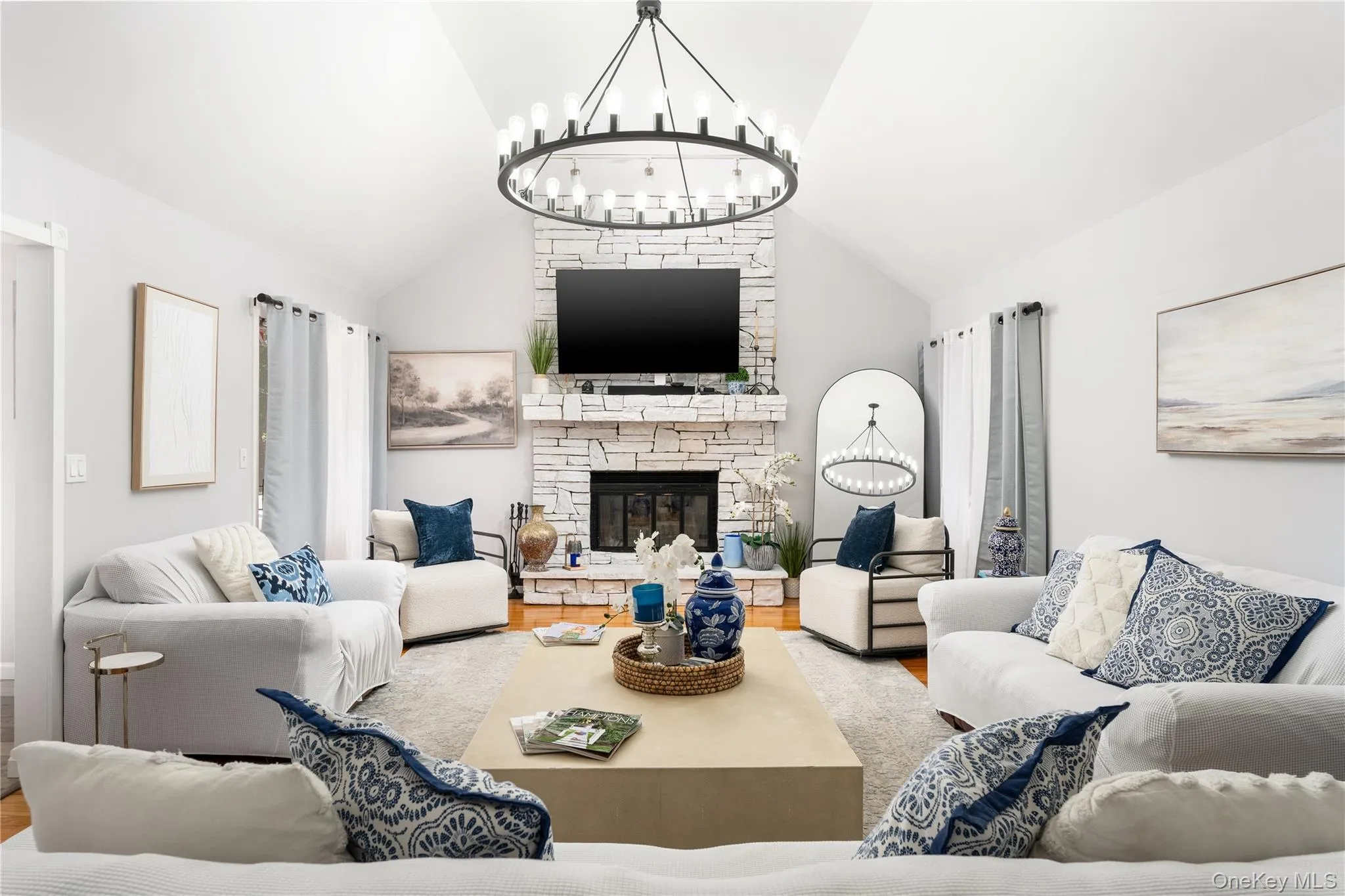 Living area featuring a stone fireplace, wood finished floors, a chandelier, and high vaulted ceiling Living area featuring a stone fireplace, wood finished floors, a chandelier, and high vaulted ceiling